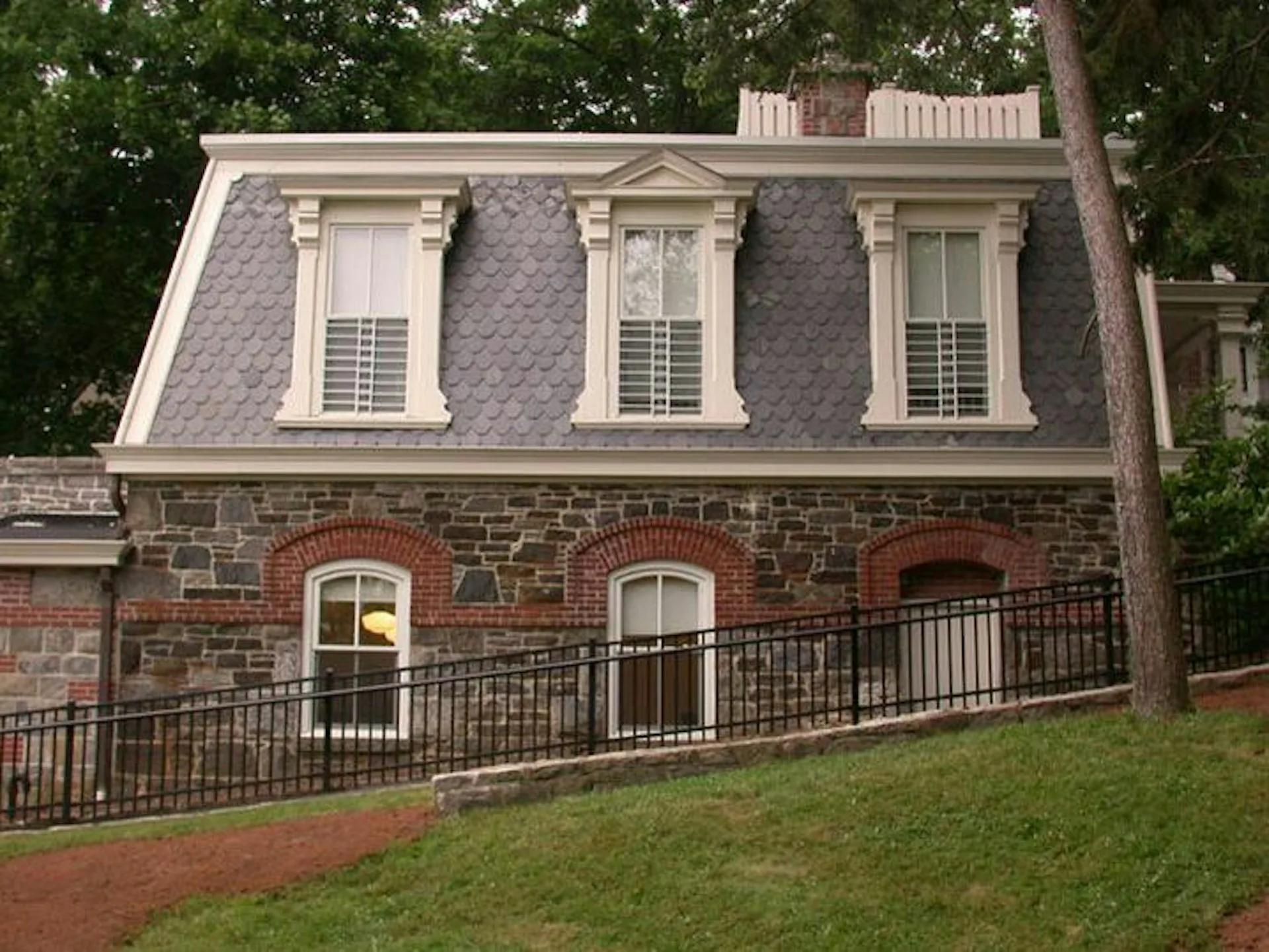 Red brick residential building with mansard roof, three dormer windows, and wrought-iron balcony railing designed by Ivan Brice Architecture.