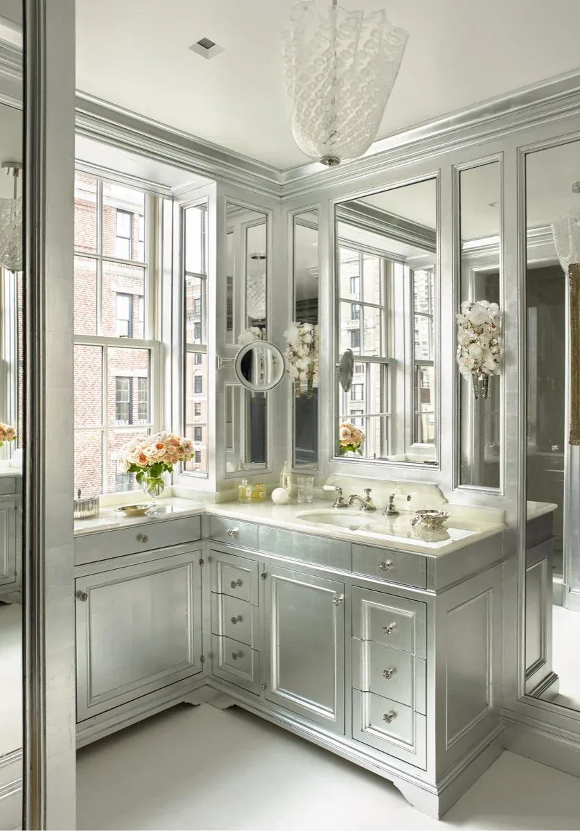 Luxurious bathroom vanity with sage-green painted cabinetry, marble countertop, and mirrored walls flooded with natural light by J. Gordon Painted Finishes.