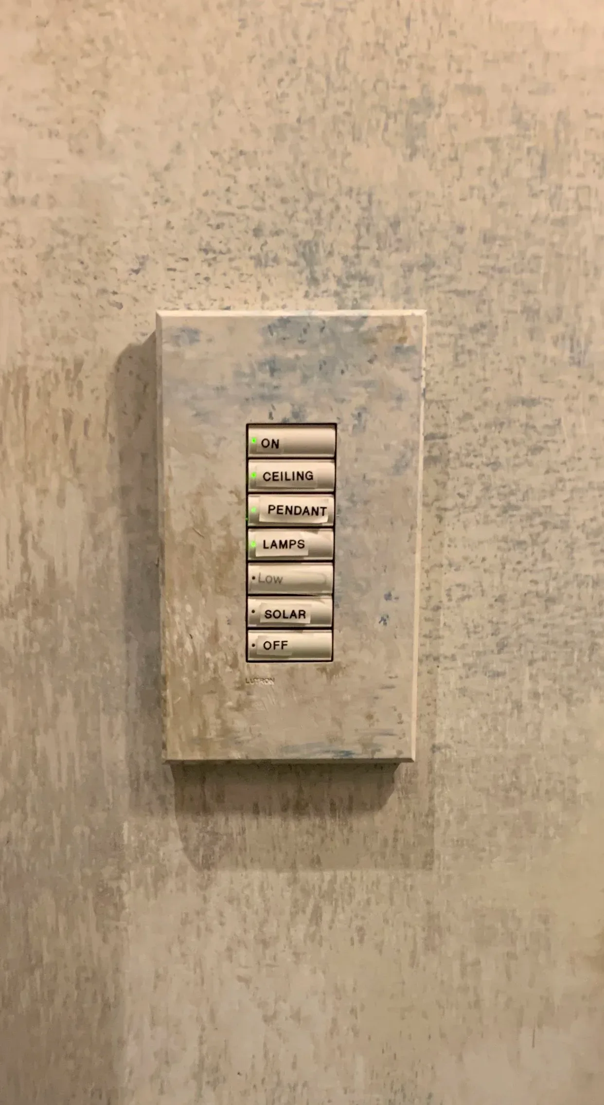 A light switch plate with multiple button controls mounted on a textured beige wall finished by J. Gordon Painted Finishes.