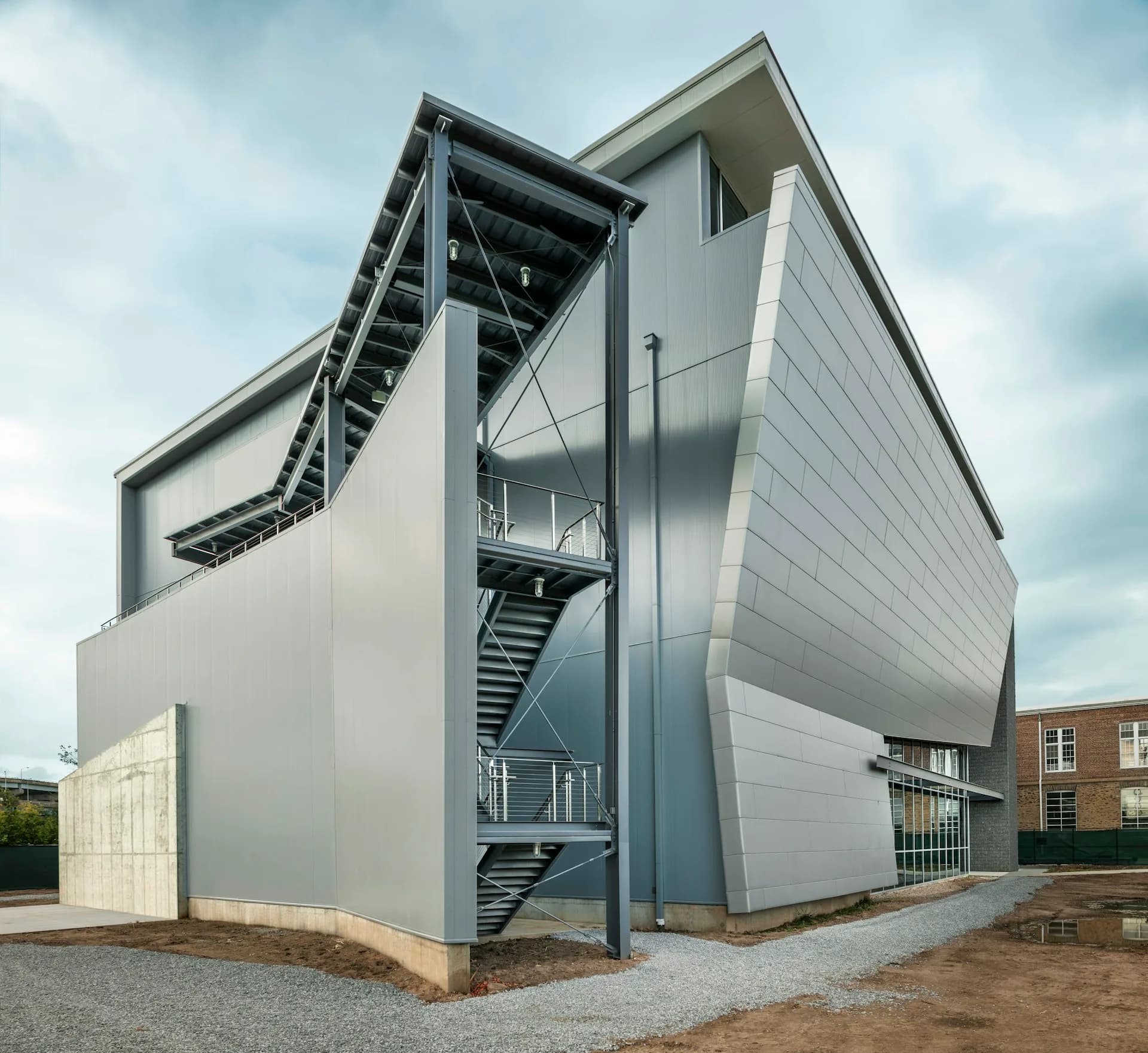 Modern white cubic building with angular metal staircase tower and geometric forms, set against cloudy sky, by Jack L. Gordon Architects.