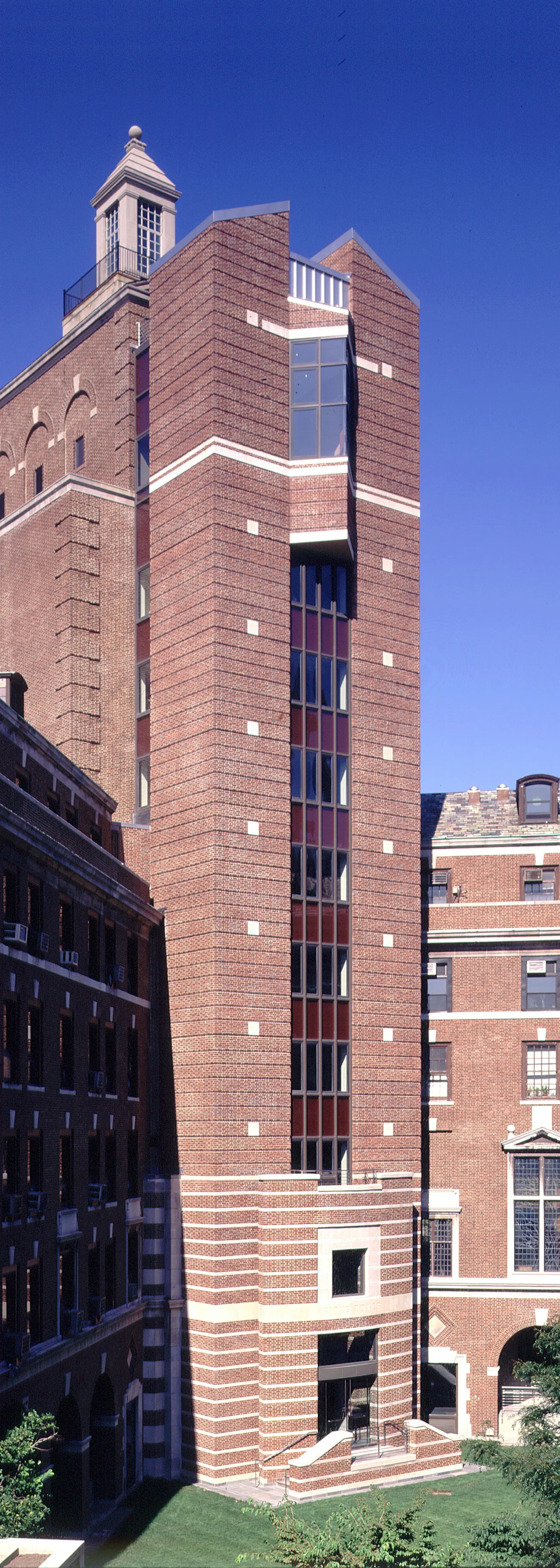 Tall brick tower with distinctive vertical window element, white trim bands, and cupola top, photographed against clear blue sky by Jack L. Gordon Architects.