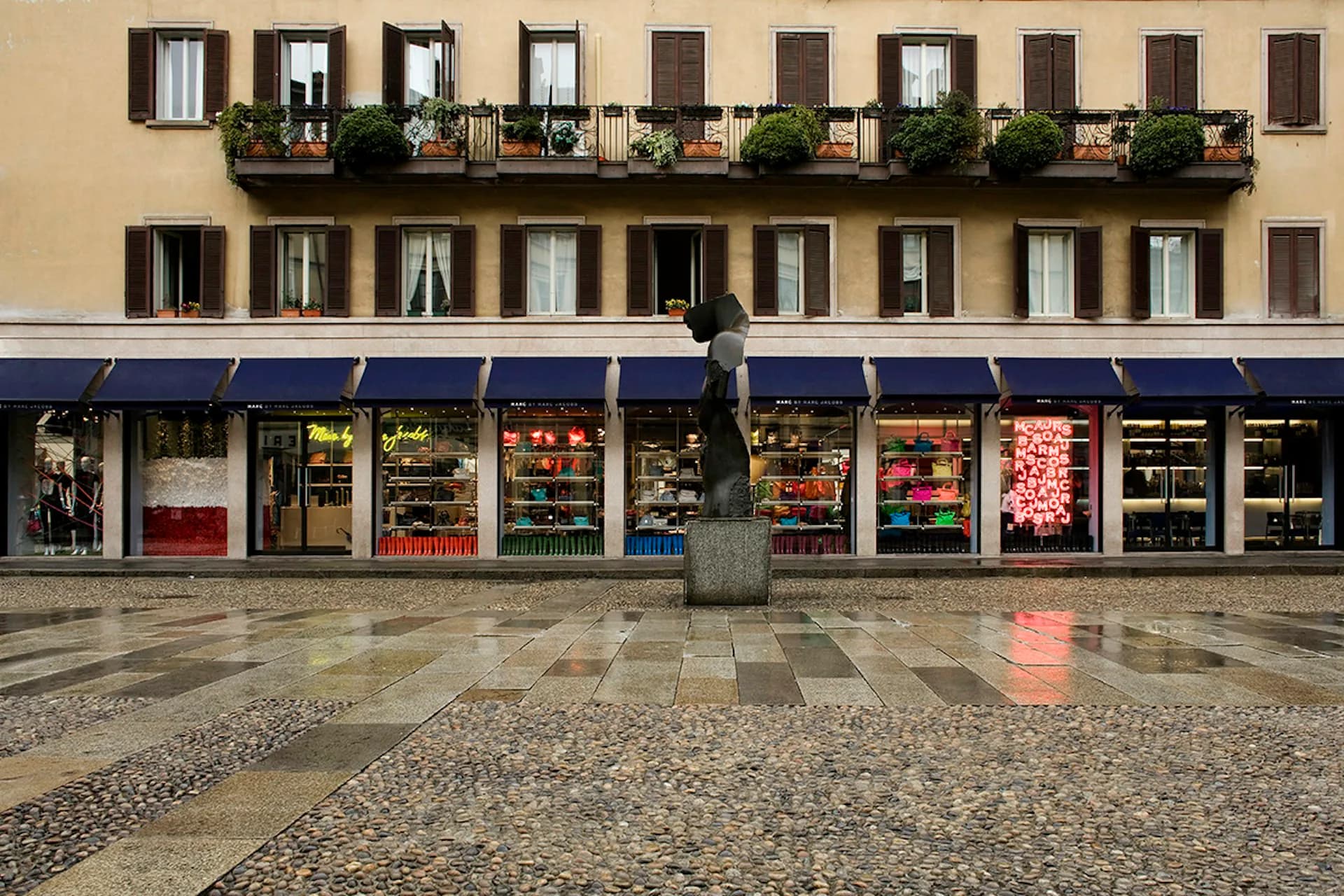 Storefront facade with ground-level retail windows and residential apartments above featuring symmetrical windows and a continuous balcony, designed by Jaklitsch / Gardner Architects.