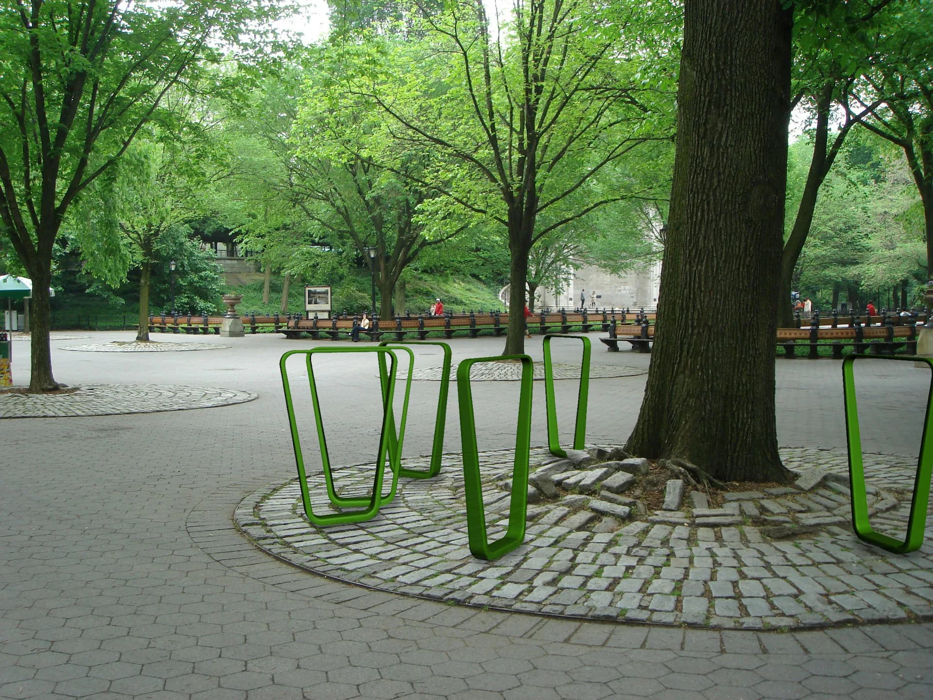 Public plaza seating area with bright green sculptural benches arranged around mature trees on paved ground, designed by Jaklitsch / Gardner Architects.