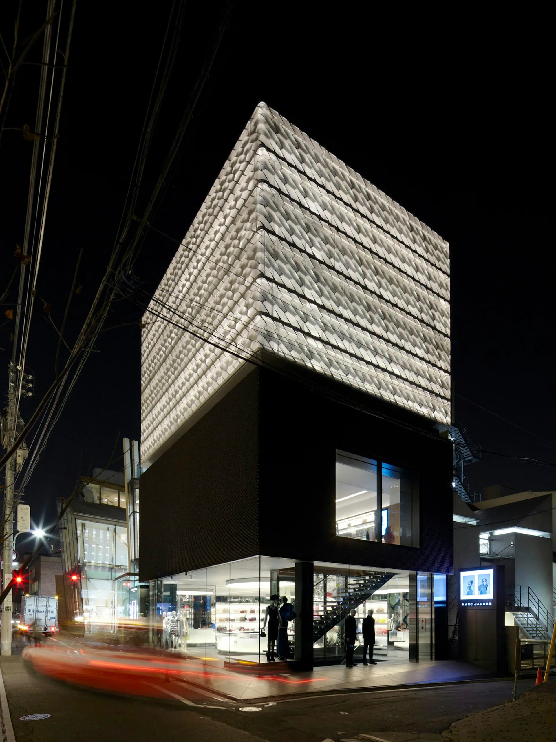 Night photograph of a modern black and white storefront with stacked brick upper facade and large glass ground-level windows, designed by Jaklitsch / Gardner Architects.