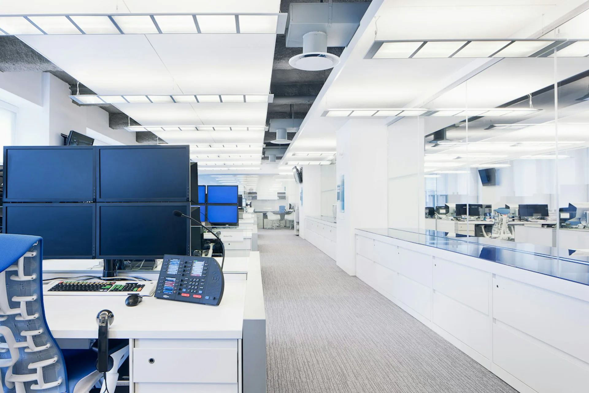 Modern laboratory or medical office interior featuring blue acoustic panels, white cabinetry, polished concrete flooring, and bright LED ceiling panels, designed by Janko Rasic Architects, PLLC.