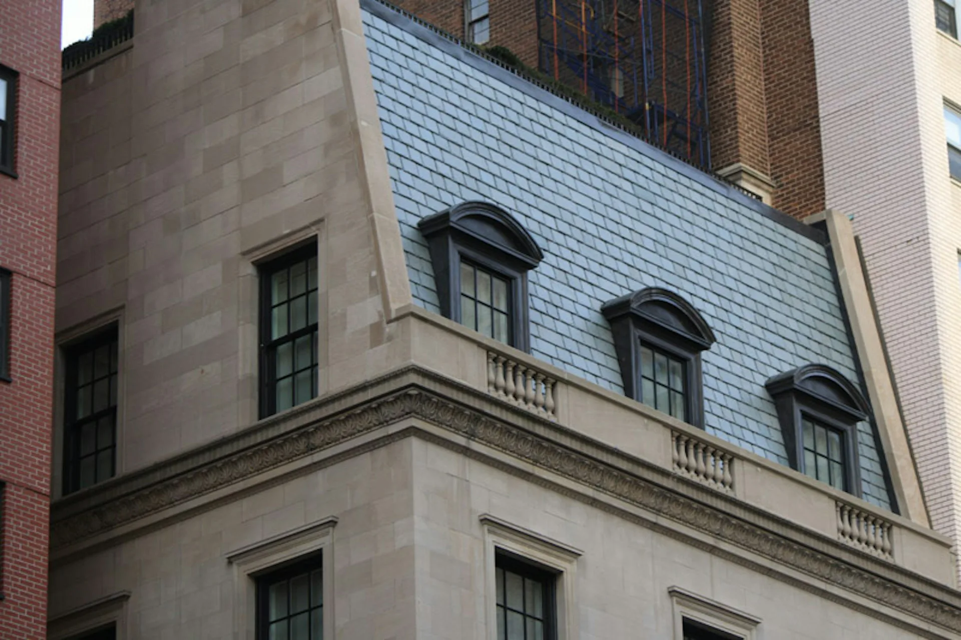 Mansard roof with blue-gray slate shingles and dormer windows on a classical stone and brick building facade by Janko Rasic Architects, PLLC.