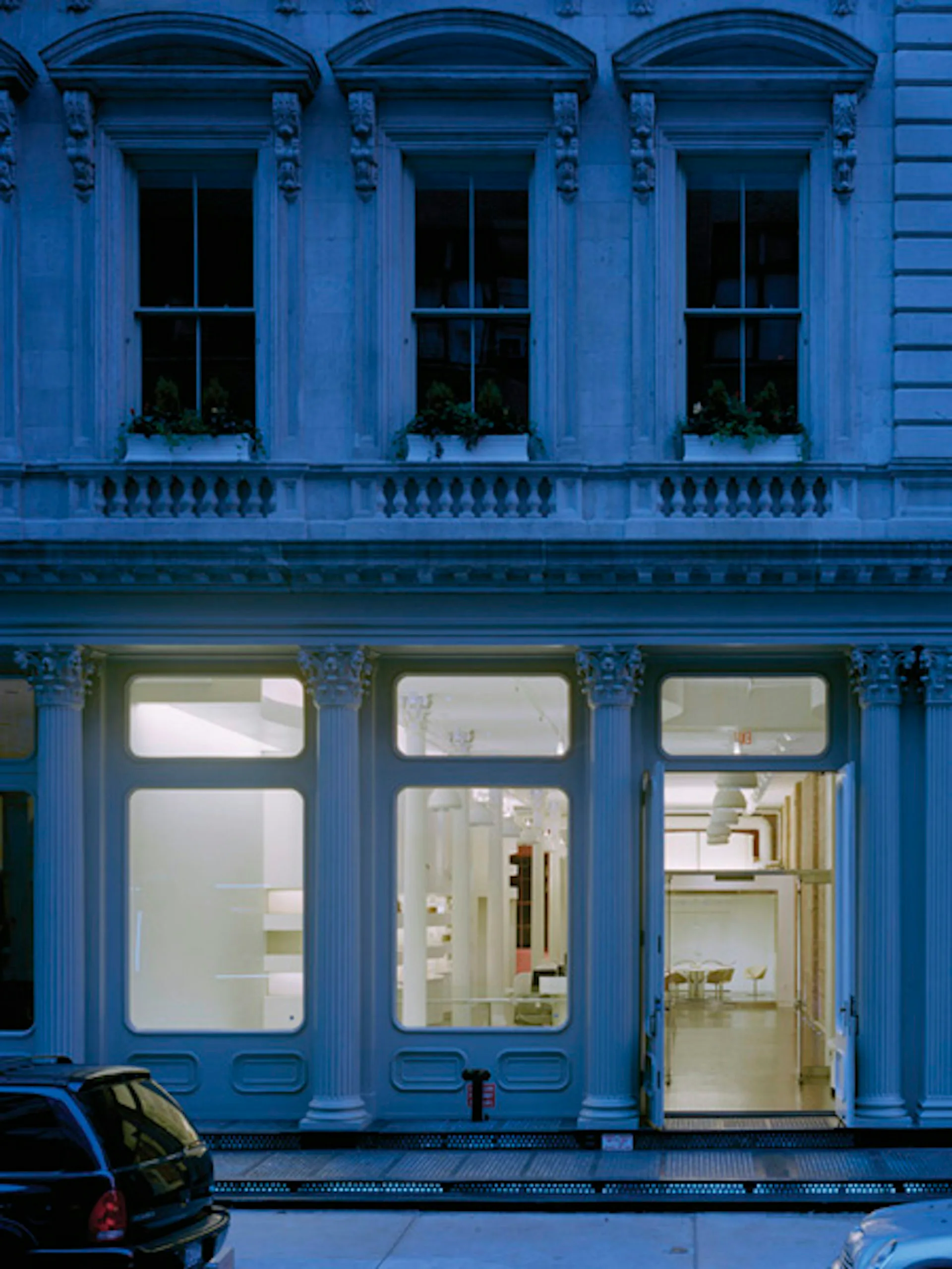Bright blue neoclassical storefront facade with three arched windows on upper level and three large glass doors on ground floor, clean modern interior visible through windows, by Janko Rasic Architects, PLLC.
