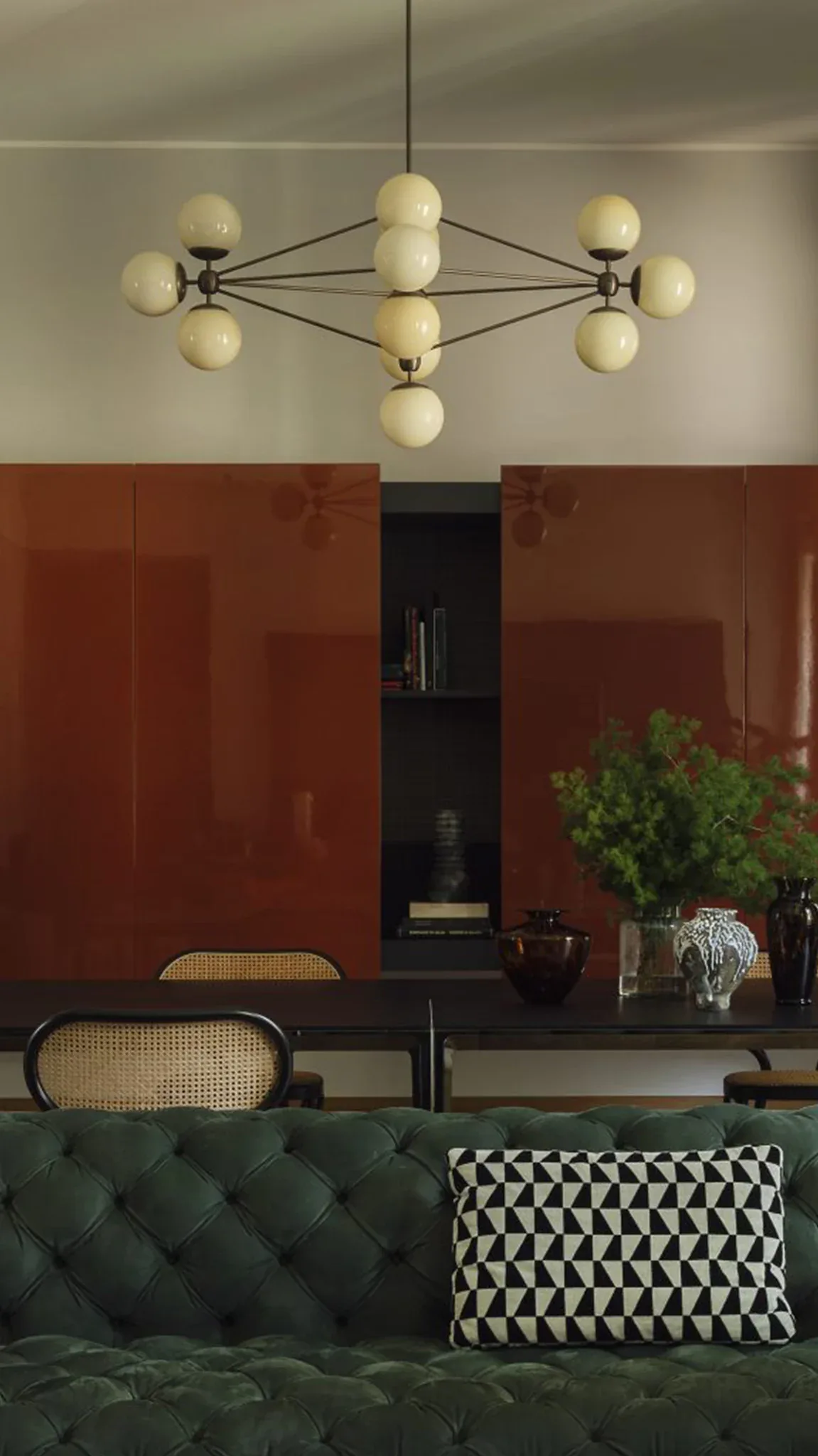 Modern living room with cream pendant chandelier, burgundy cabinetry, green tufted sofa, and monochromatic geometric pillow by Jason Miller Studio.
