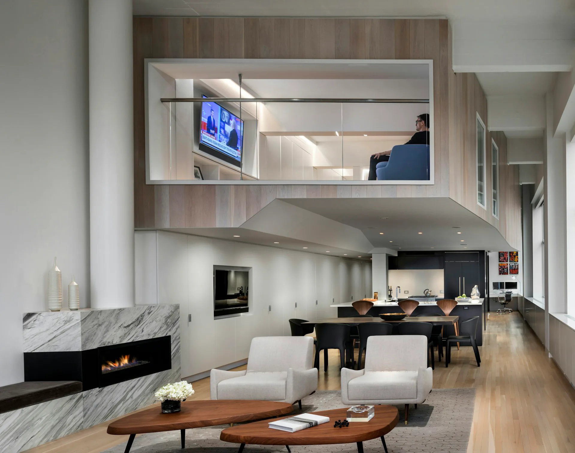 Modern loft interior with double-height ceiling, marble fireplace, white seating, dining area, and mezzanine office space with blue accent wall by Joel Sanders Architect.