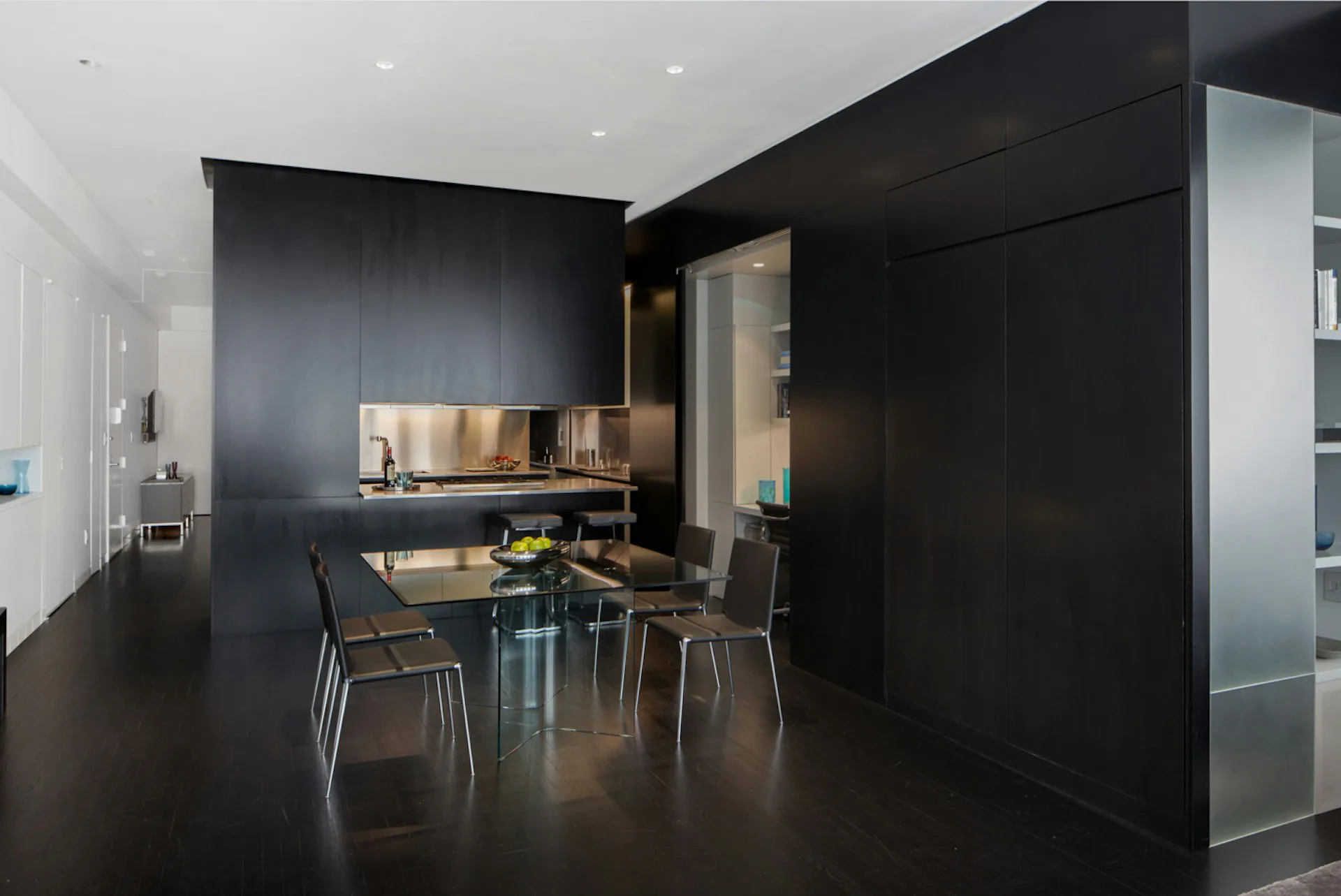 Modern black-walled apartment kitchen and dining area with metallic accents, concrete flooring, and minimalist furnishings by Joel Sanders Architect.