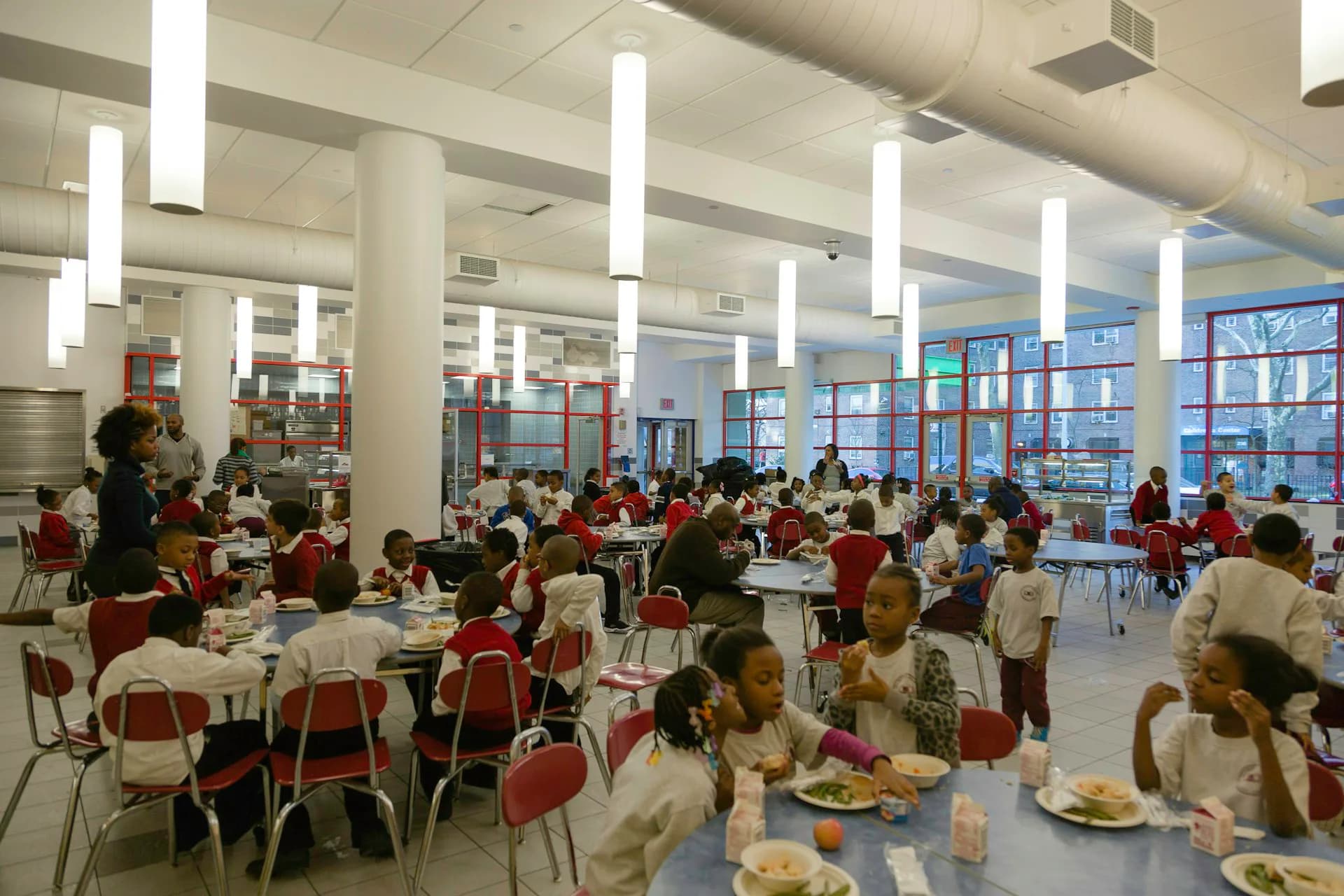 Modern school cafeteria with red chairs, long tables, and natural light from large windows, designed by Ciardullo A&E.
