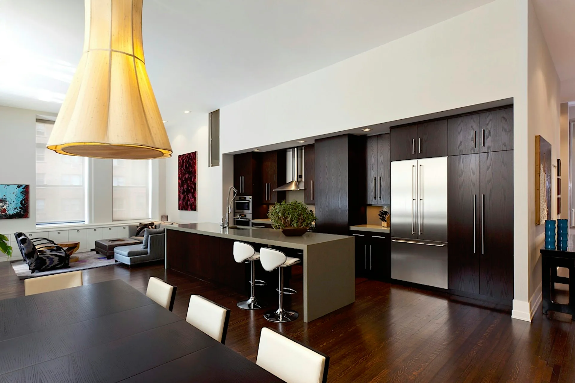 Contemporary kitchen with dark cabinetry, stainless steel appliances, light wood pendant lighting, and connected dining area with white chairs by Jonathan B. Held A.I.A. Architect.