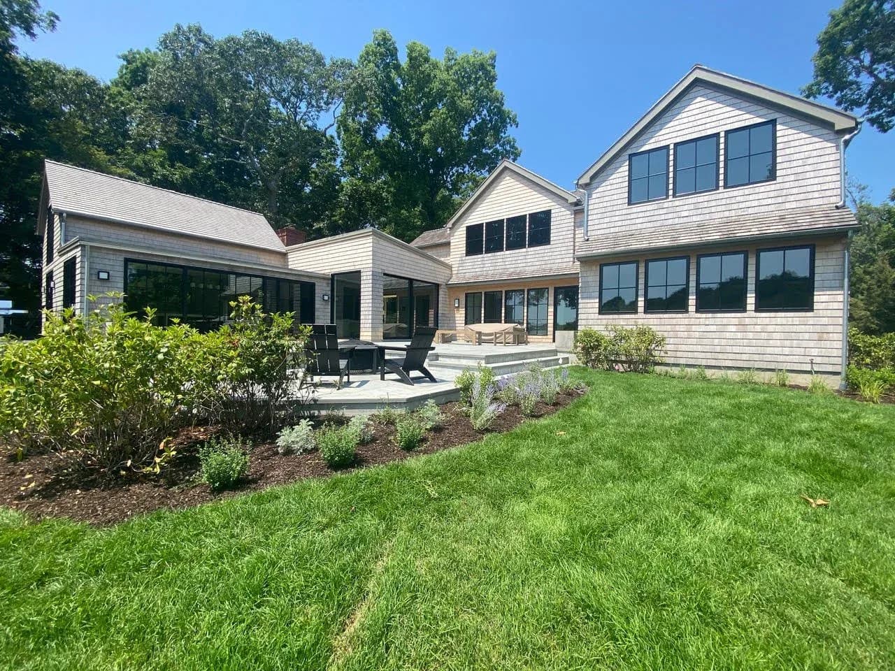 Modern residential home exterior featuring white siding, multiple gabled rooflines, and expansive windows overlooking manicured lawn and landscaping by Jonathan B. Held A.I.A. Architect.