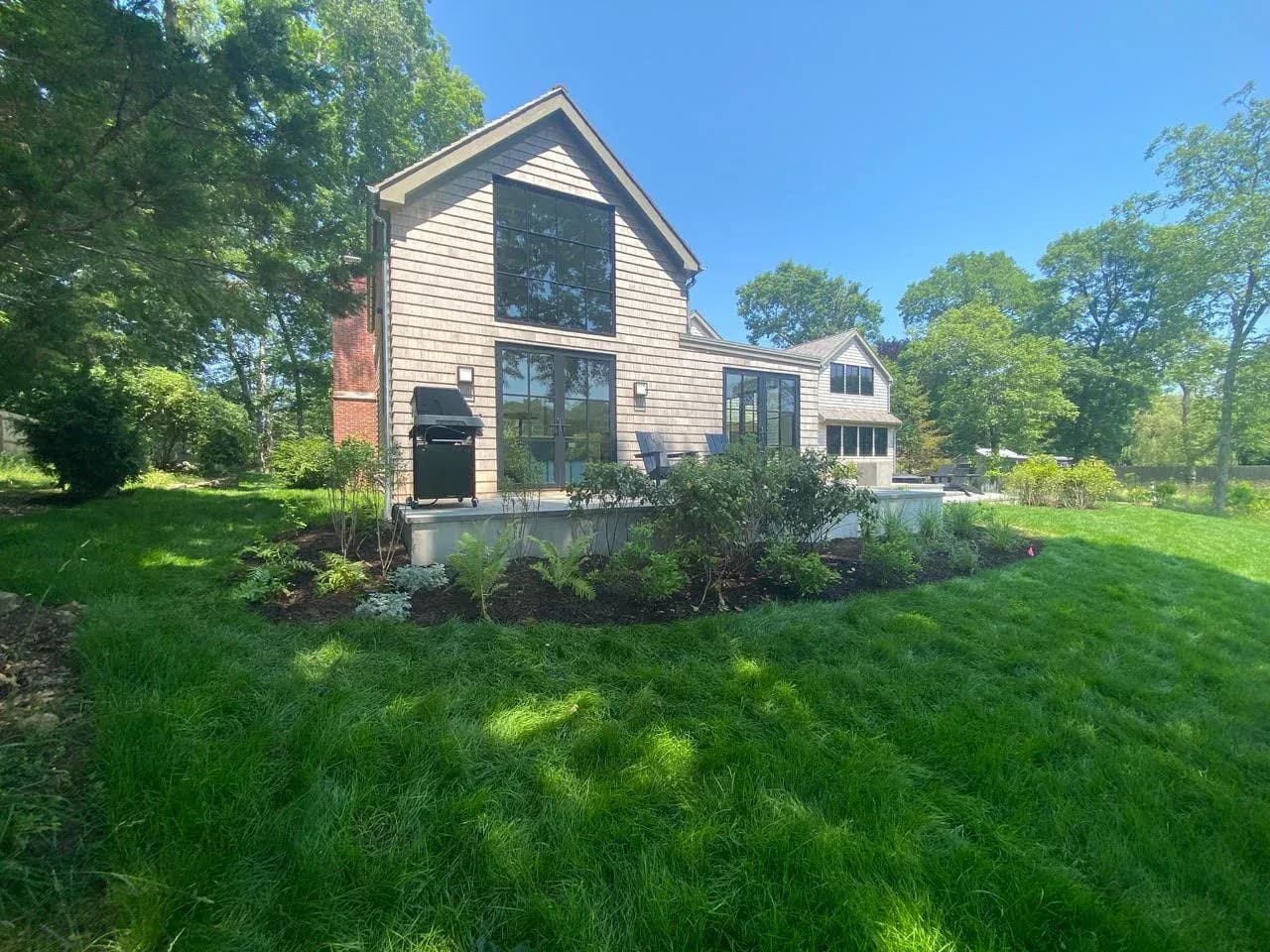 Modern residential home with board-and-batten siding, large gable windows, and expansive lawn surrounded by mature trees by Jonathan B. Held A.I.A. Architect
