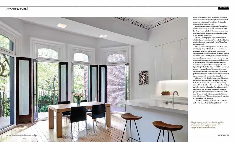 Bright minimalist kitchen and dining space with wood table, black chairs, white cabinetry, and glass doors opening to garden by julian king architect.