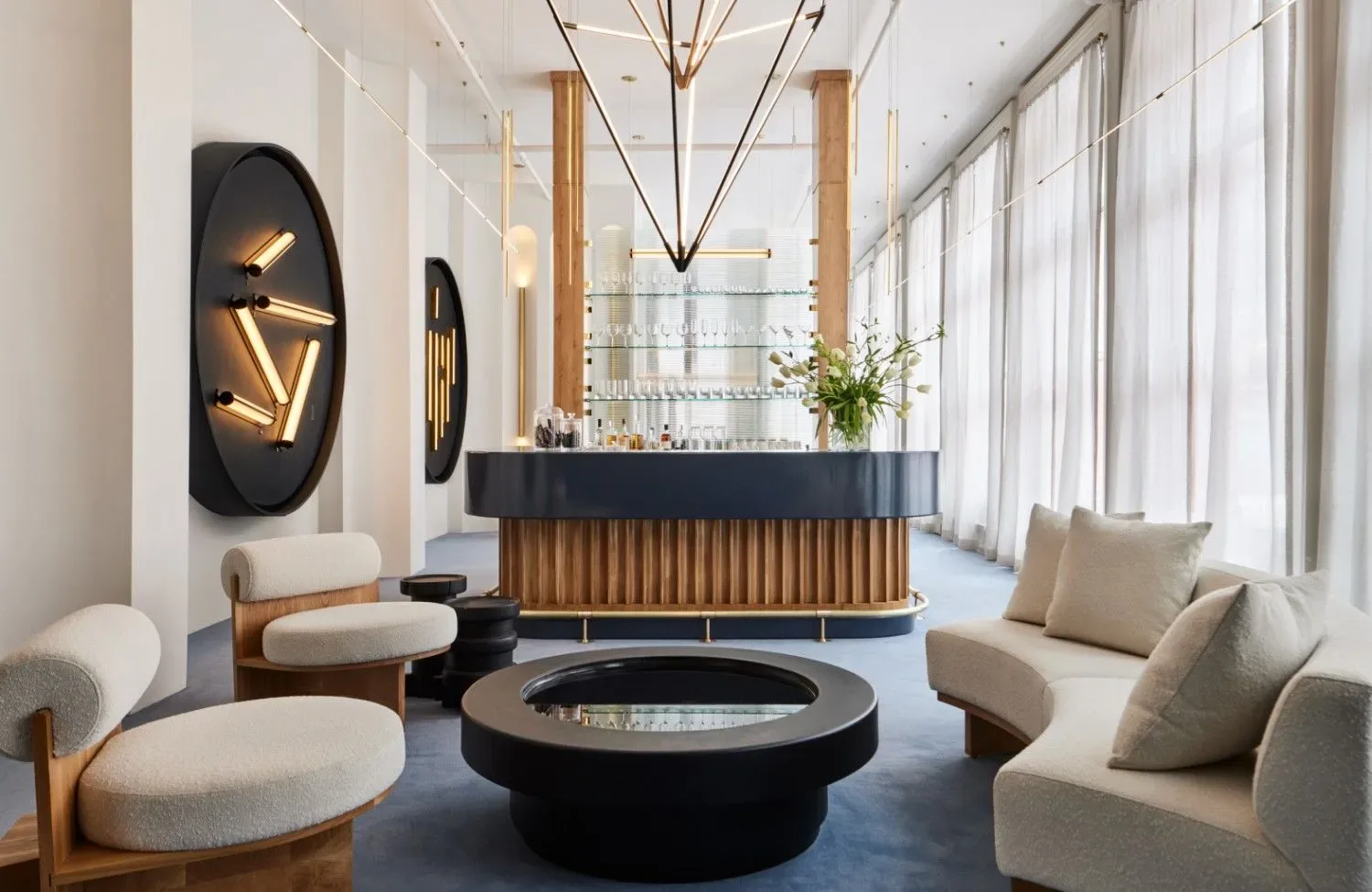 Modern hotel lobby with cream seating, black fireplace, wood-paneled reception desk, neon wall art, and floor-to-ceiling windows by Juniper Design.