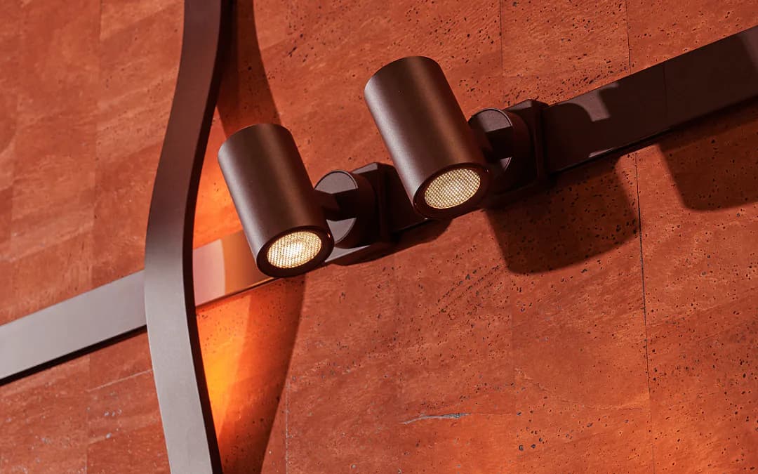 Architectural lighting installation featuring three cylindrical bronze fixtures mounted on a terracotta textured wall, casting warm light and shadows by Juniper Design.
