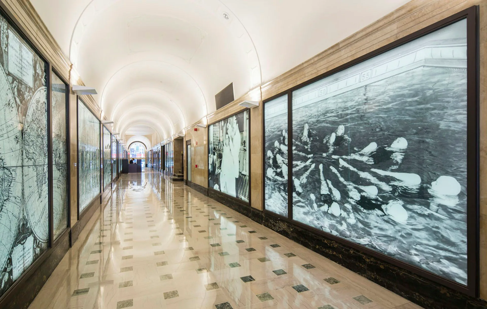 Long gallery corridor with arched ceiling, marble walls, polished terrazzo floor, and framed black-and-white photographs displayed along both sides by Kahn Architecture & Design, PC.