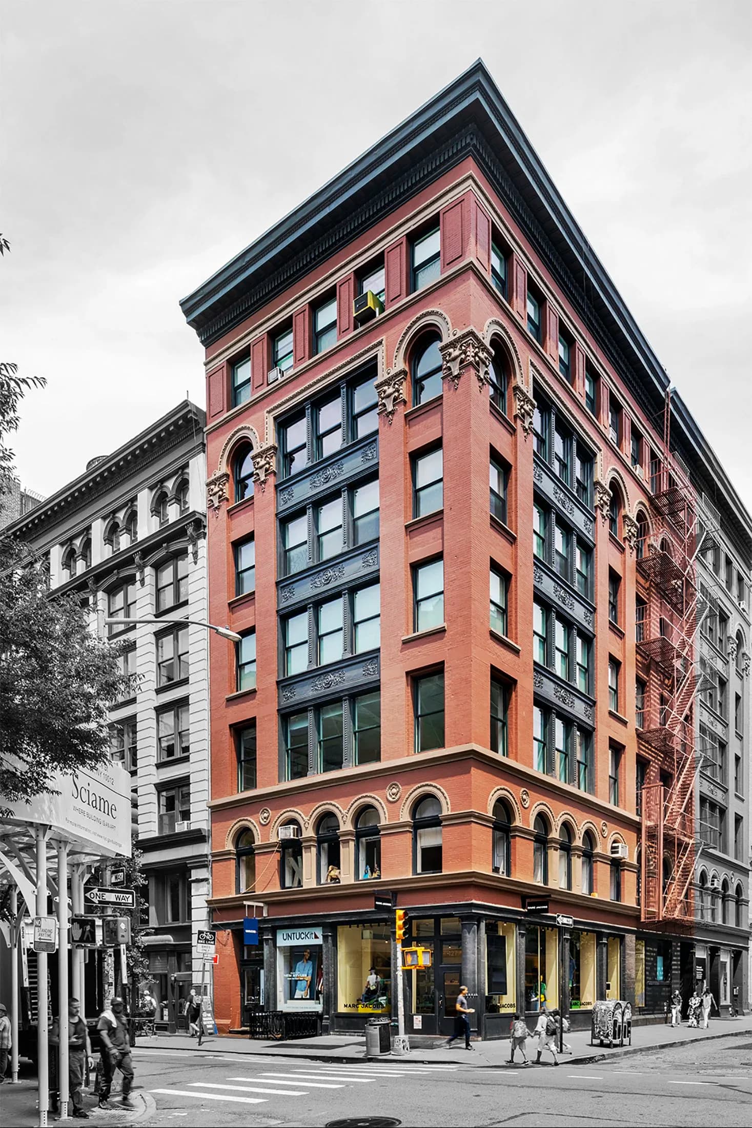 Red brick historic corner building with ornate arched windows and dark cornice detail, photographed in selective color by Katz Architecture.