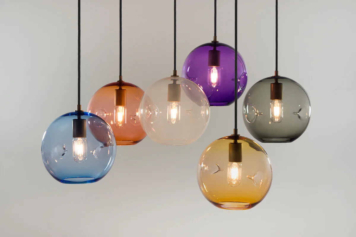 Pendant lighting installation featuring six suspended glass spheres in blue, orange, cream, purple, amber, and gray tones with warm filament bulbs by KEEP.