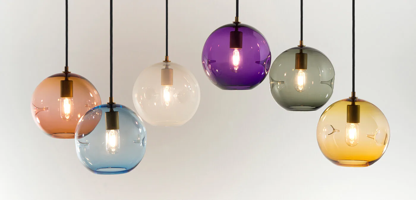 Colorful pendant lighting fixtures in orange, blue, clear, purple, gray, and amber glass suspended from ceiling by KEEP.