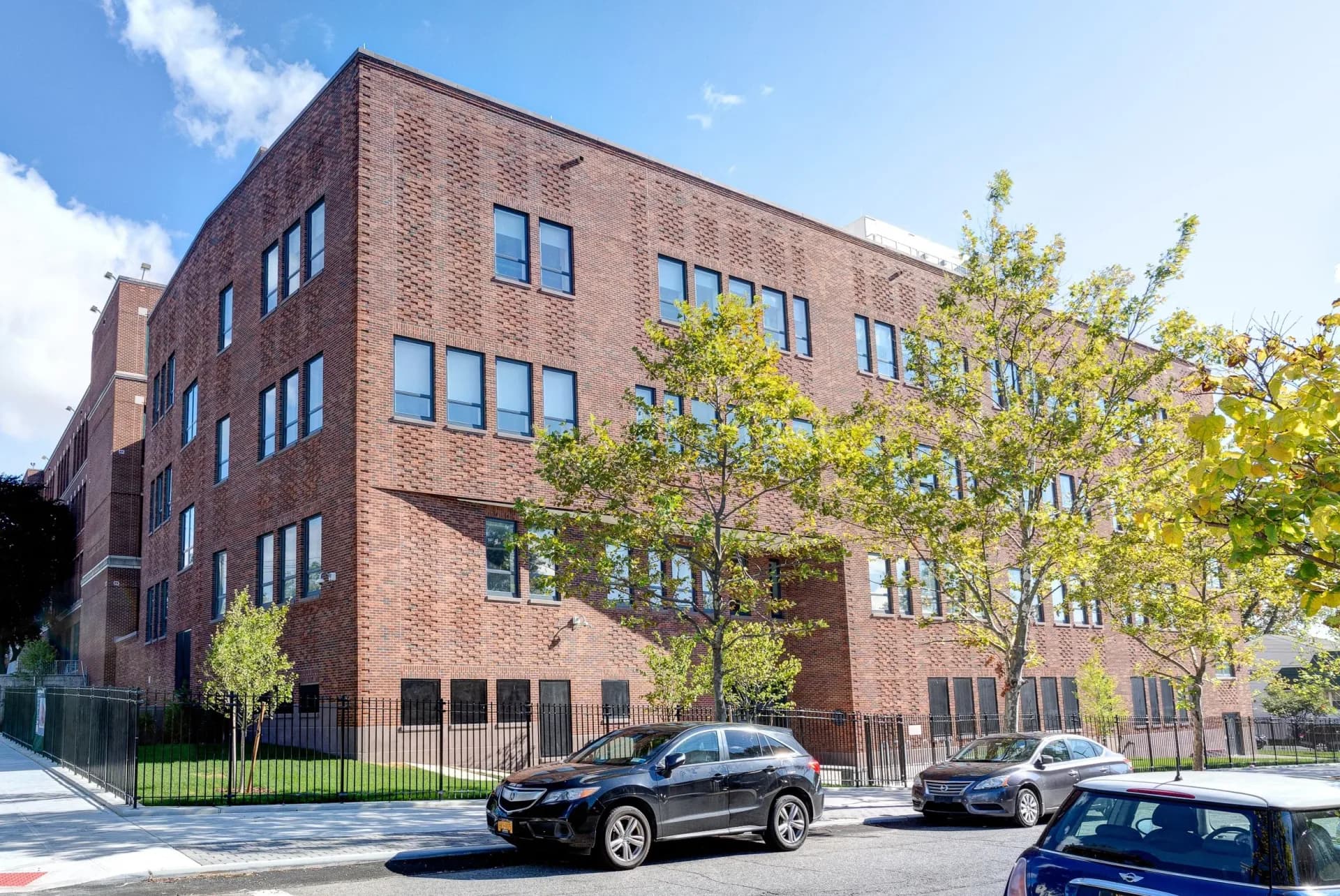 Modern brick residential building with ground-floor commercial spaces, featuring large windows and green landscaping, designed by Kenny & Khan Architects PC.