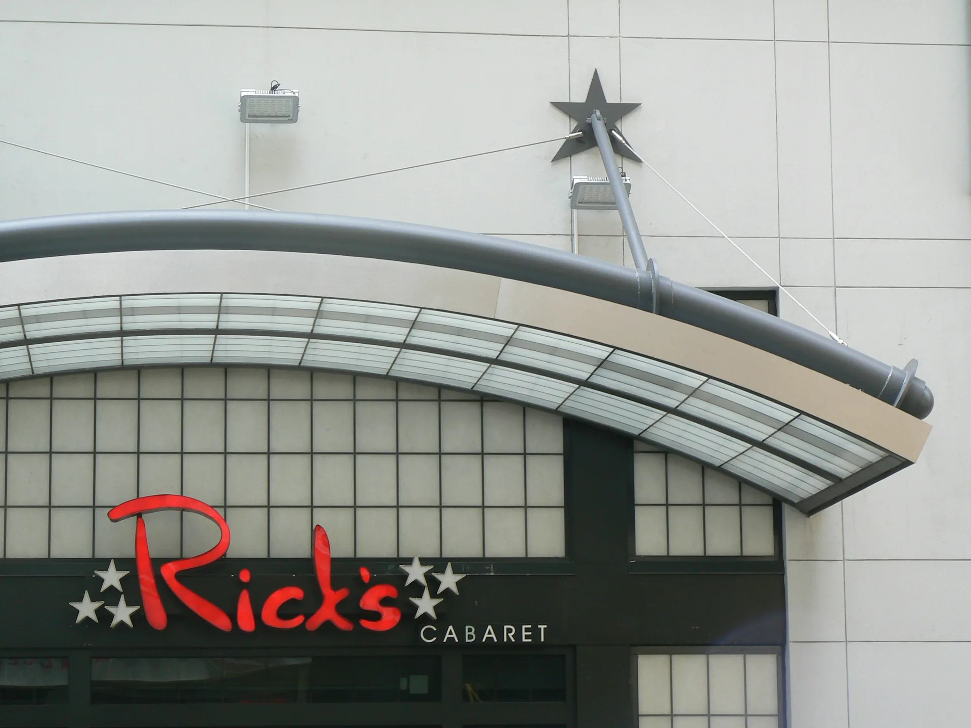 Rick's Cabaret nightclub exterior featuring curved metallic canopy with neon red signage and decorative star, designed by Kleinmann Architects.