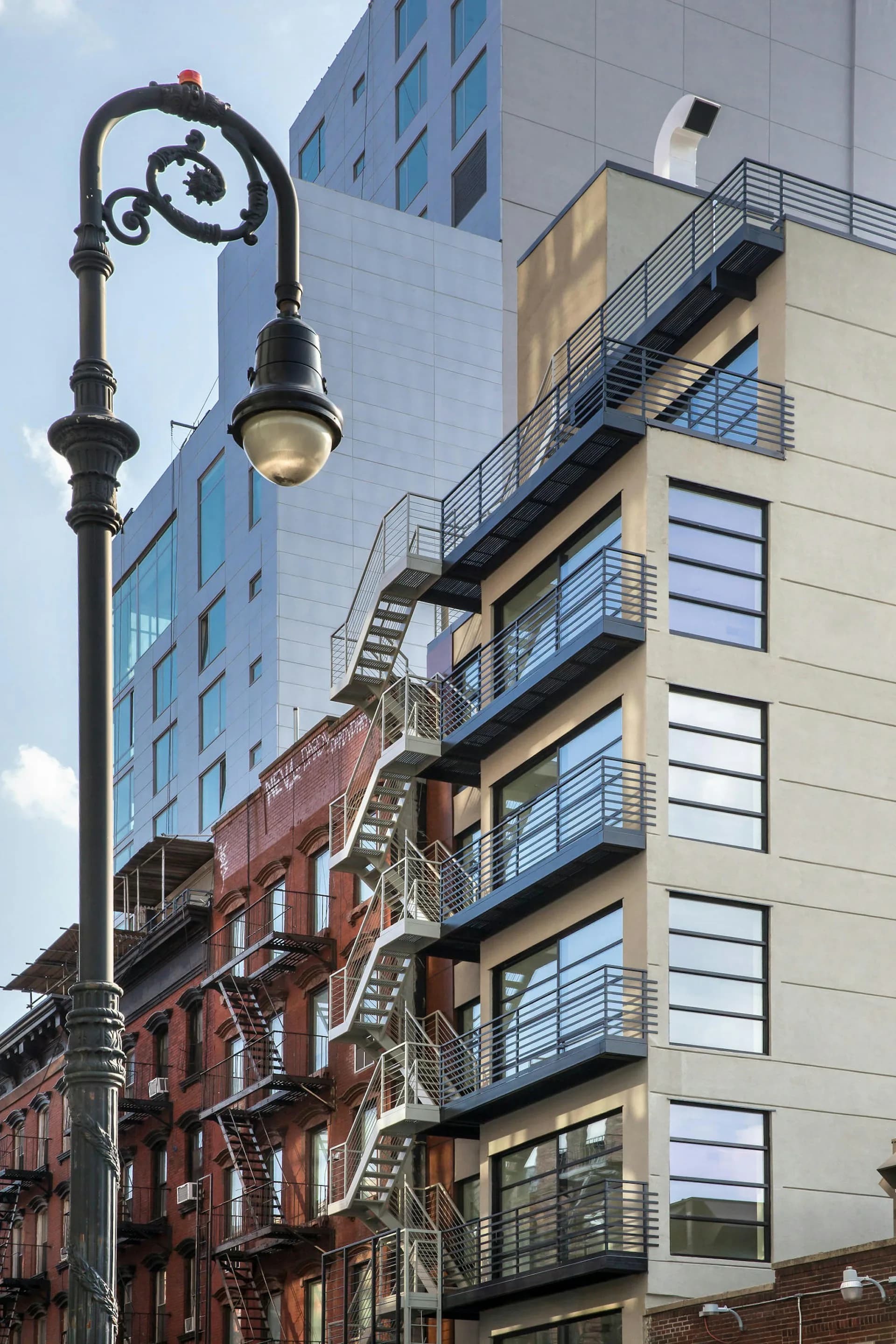 Urban streetscape featuring ornate vintage street lamp against contrasting red brick and modern glass buildings with metal fire escapes by Kleinmann Architects.