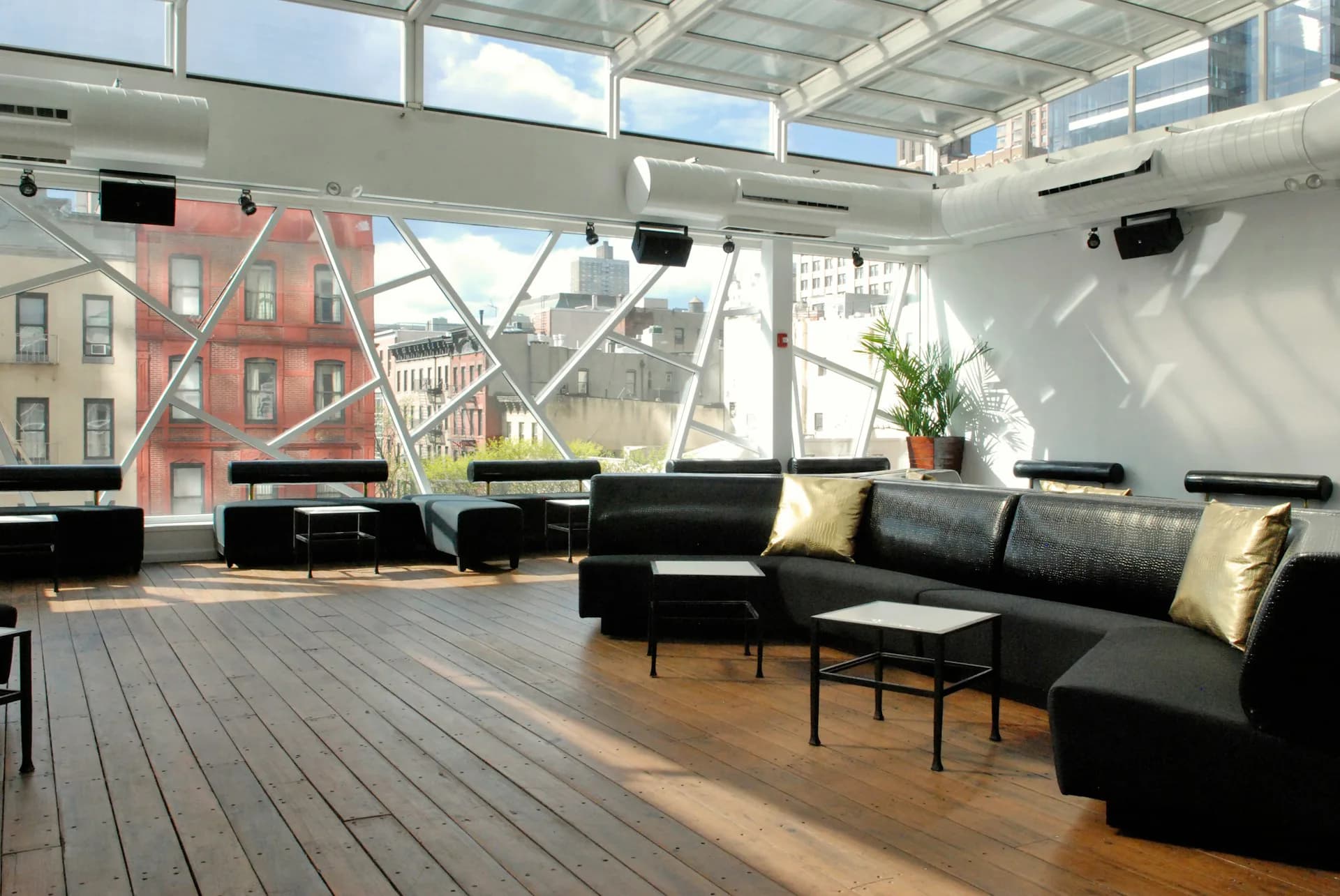 Modern loft interior with floor-to-ceiling windows, black modular seating, wooden flooring, and city views, designed by Kleinmann Architects.