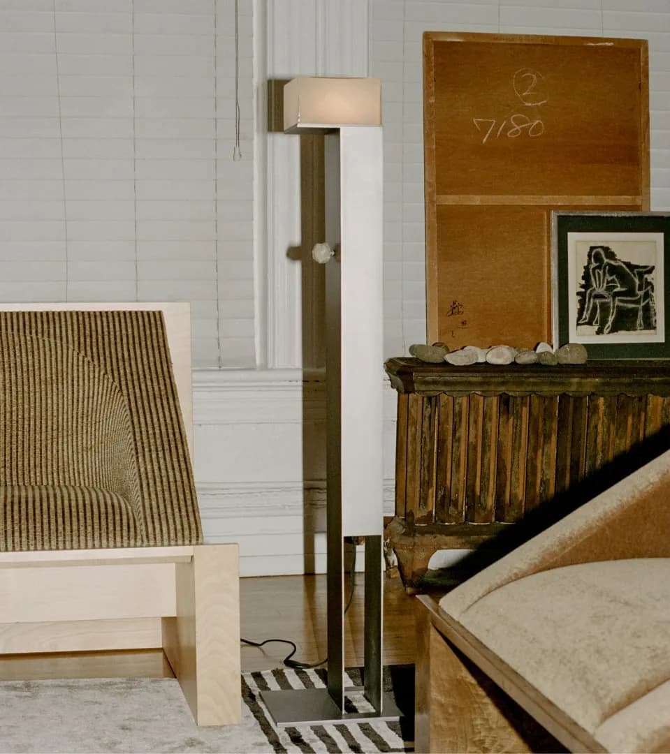 Minimalist bedroom interior featuring light wood furniture, a striped accent chair, floor lamp with cream shade, and artwork on wooden dresser, by Known Work.