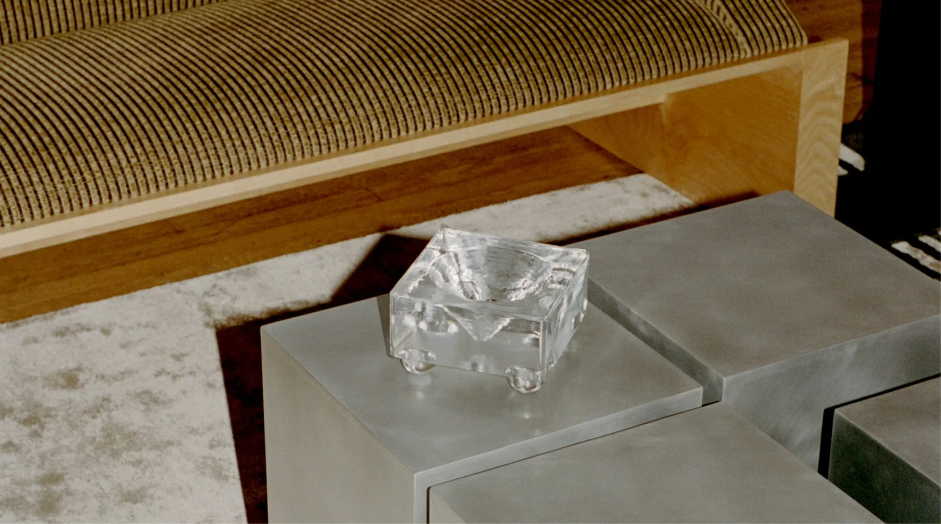 Minimalist interior with concrete side table featuring a clear glass sculptural object, positioned beside a wood-framed sofa with striped upholstery by Known Work.