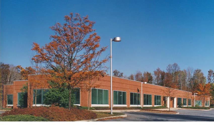 Contemporary single-story brick building with green-framed windows set among autumn trees and landscaping, designed by Koenen Associates.