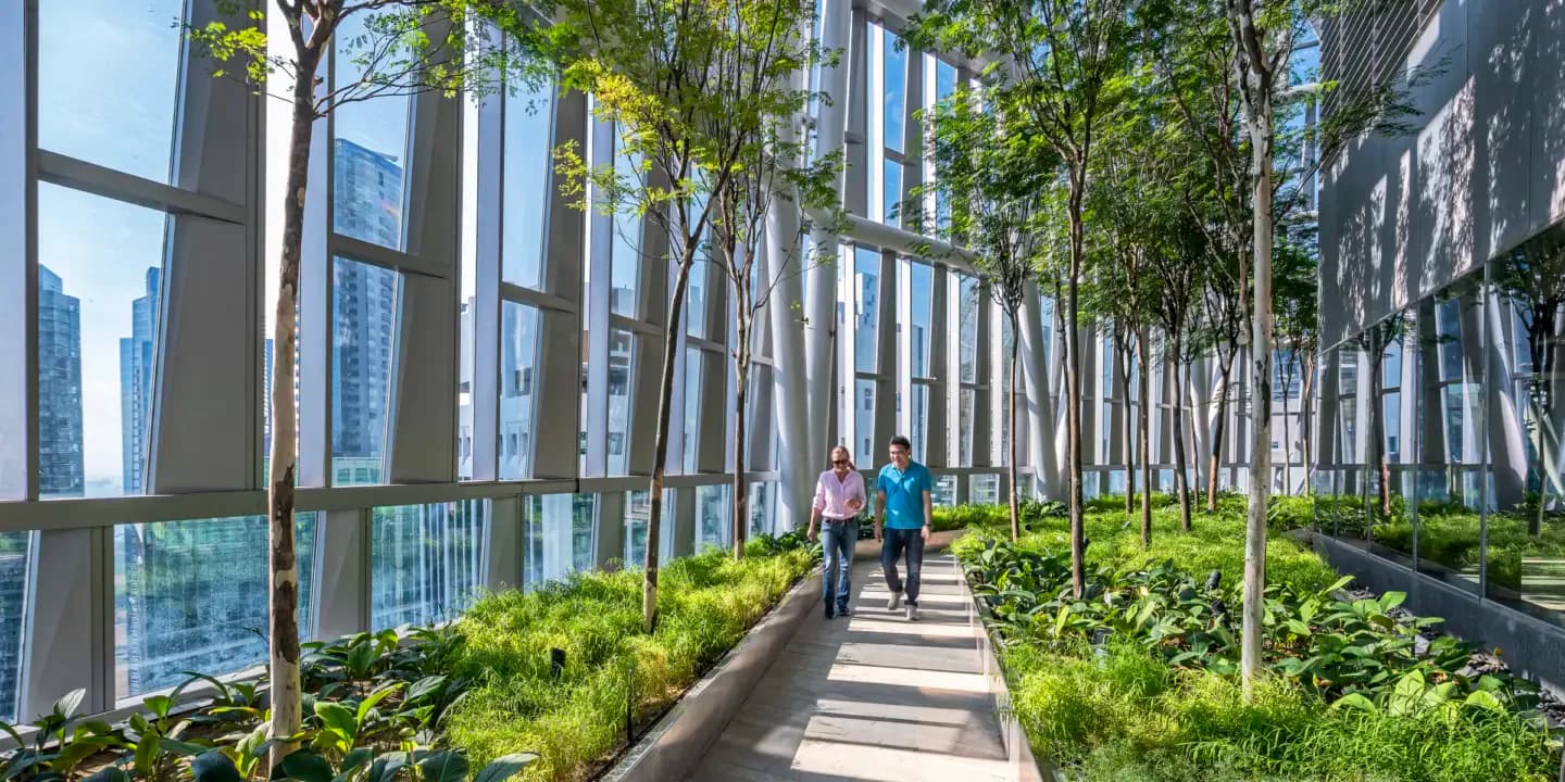 A modern outdoor corridor lined with tall trees and lush plantings between glass and metal buildings, with pedestrians walking through dappled sunlight by Kohn Pedersen Fox.