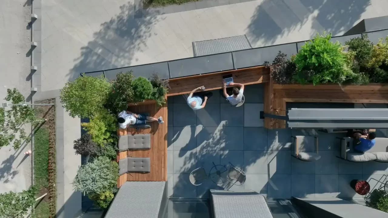 Aerial view of a modern rooftop terrace with wooden planters, paved surfaces, and synthetic trees casting precise shadows, by Komoni Architecture.
