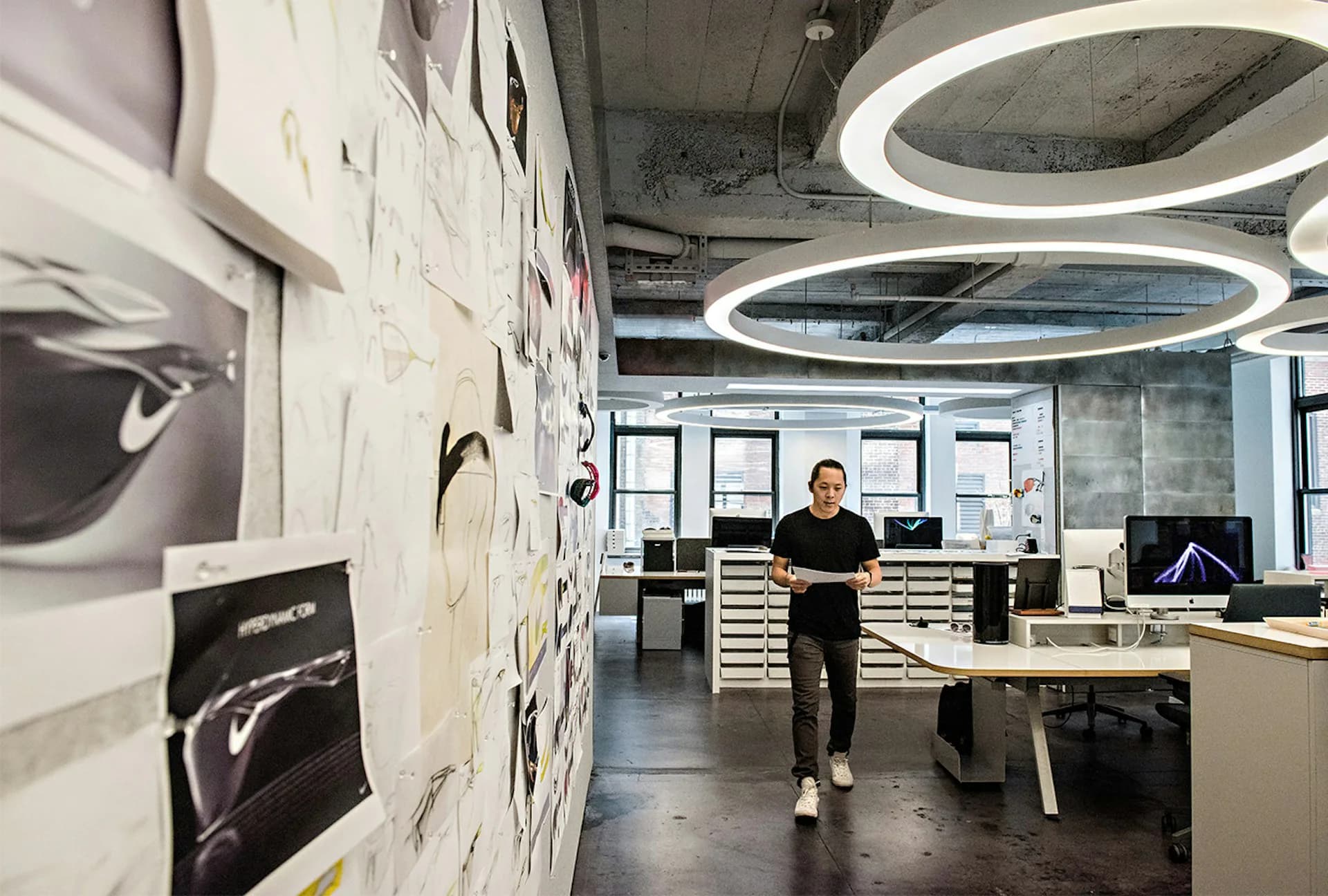 Modern open-plan office with concrete floors, white desks, circular ceiling lights, and sketch boards on walls by Kostow Greenwood Architects.