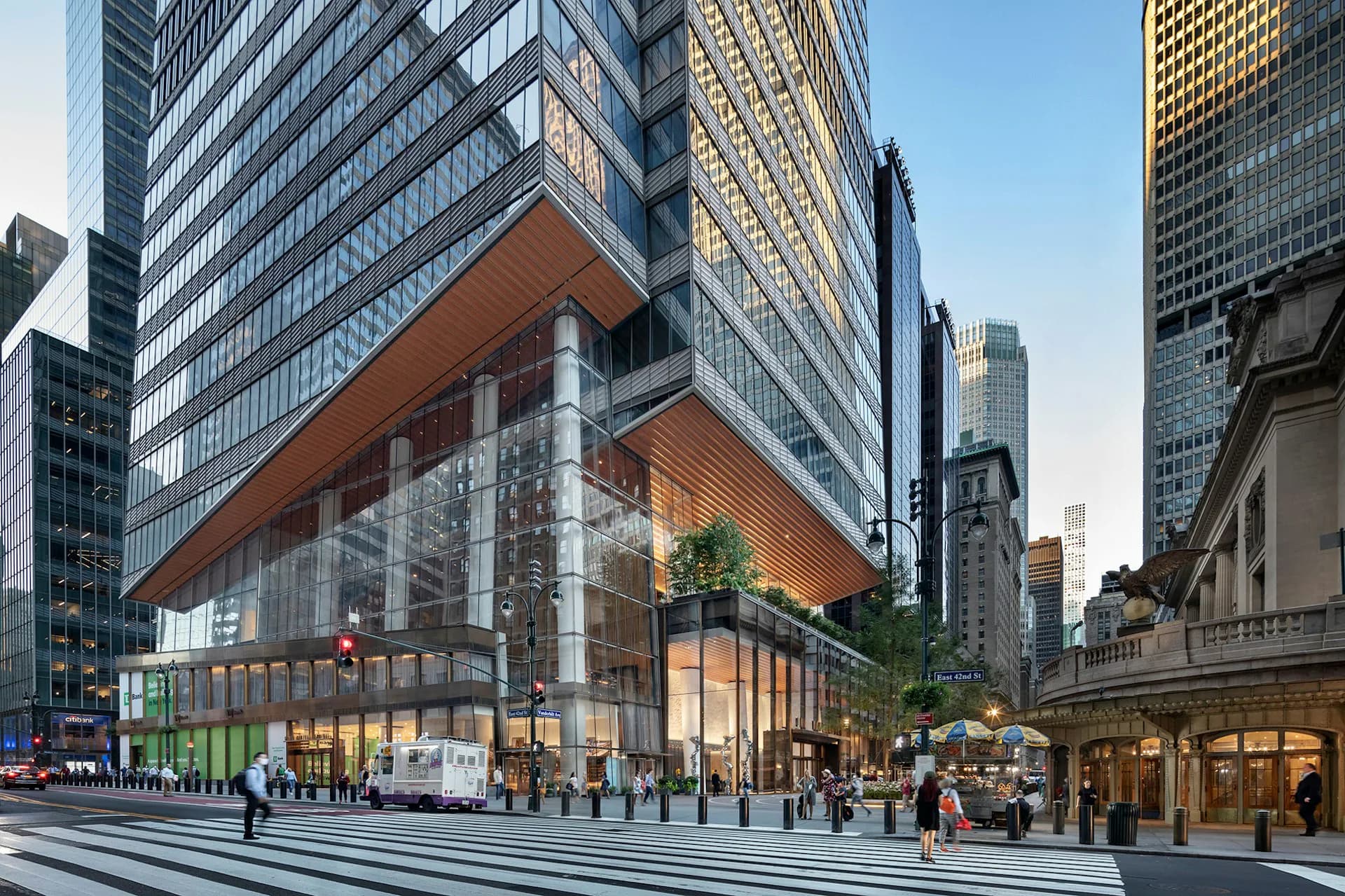 Modern mixed-use tower with illuminated ground-level retail and glazed facade overlooking a plaza with pedestrians and crosswalk by KPF (Kohn Pedersen Fox).