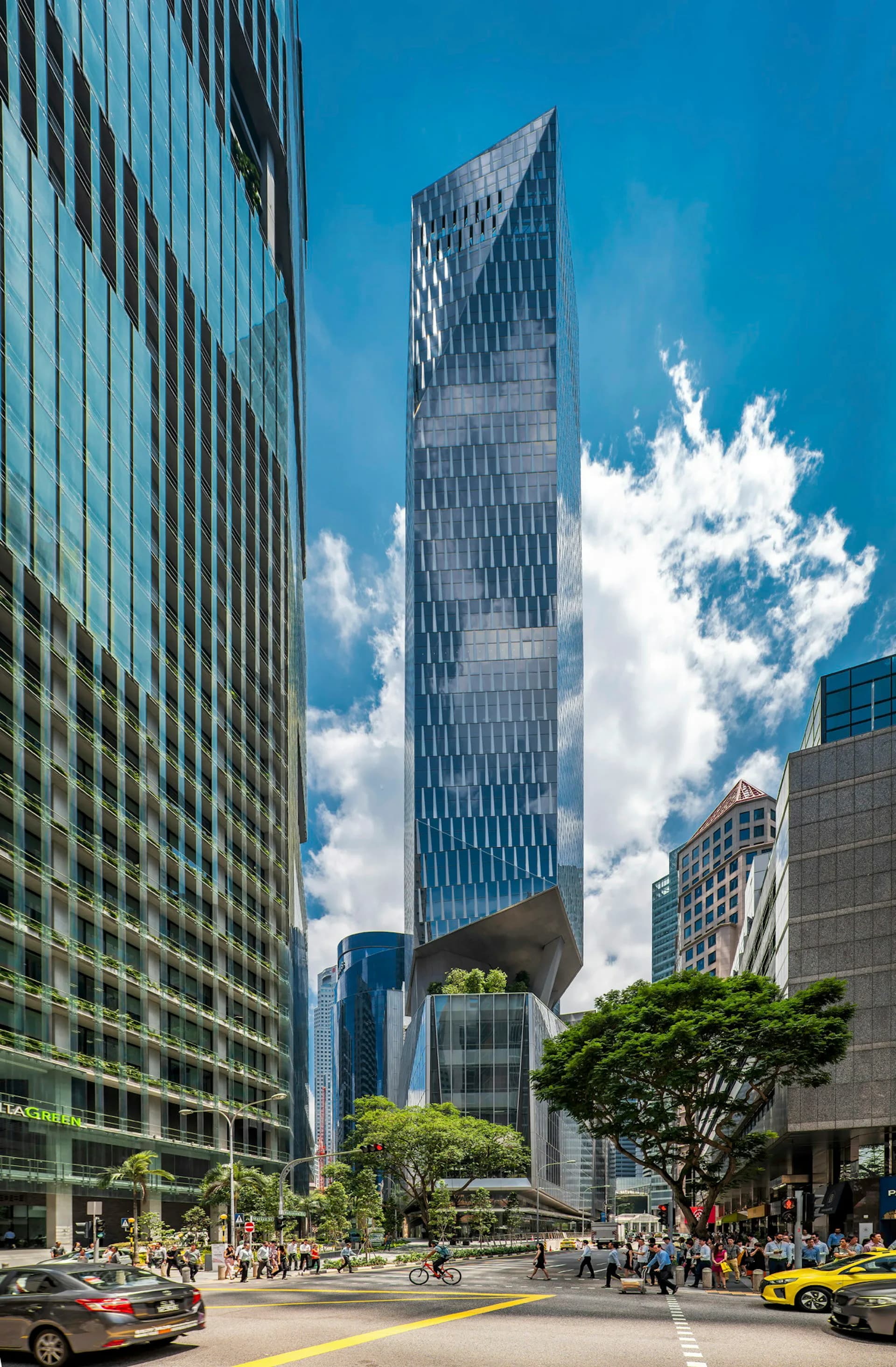 Modern urban plaza with tall residential tower, green-screened building, and mature trees against blue sky, designed by KPF (Kohn Pedersen Fox).