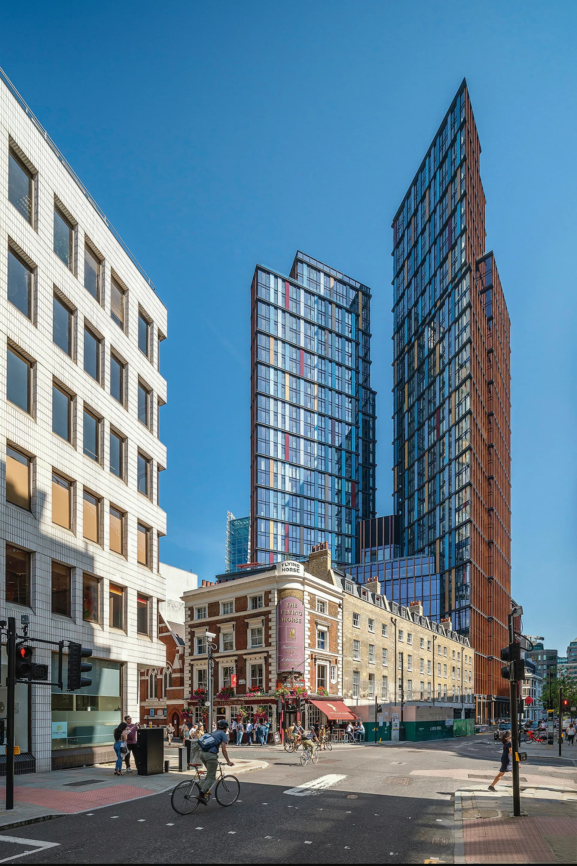 Urban street plaza with mixed-height buildings featuring white modern facades, historic brick structures, and contemporary glass towers under clear blue sky by KPF (Kohn Pedersen Fox).