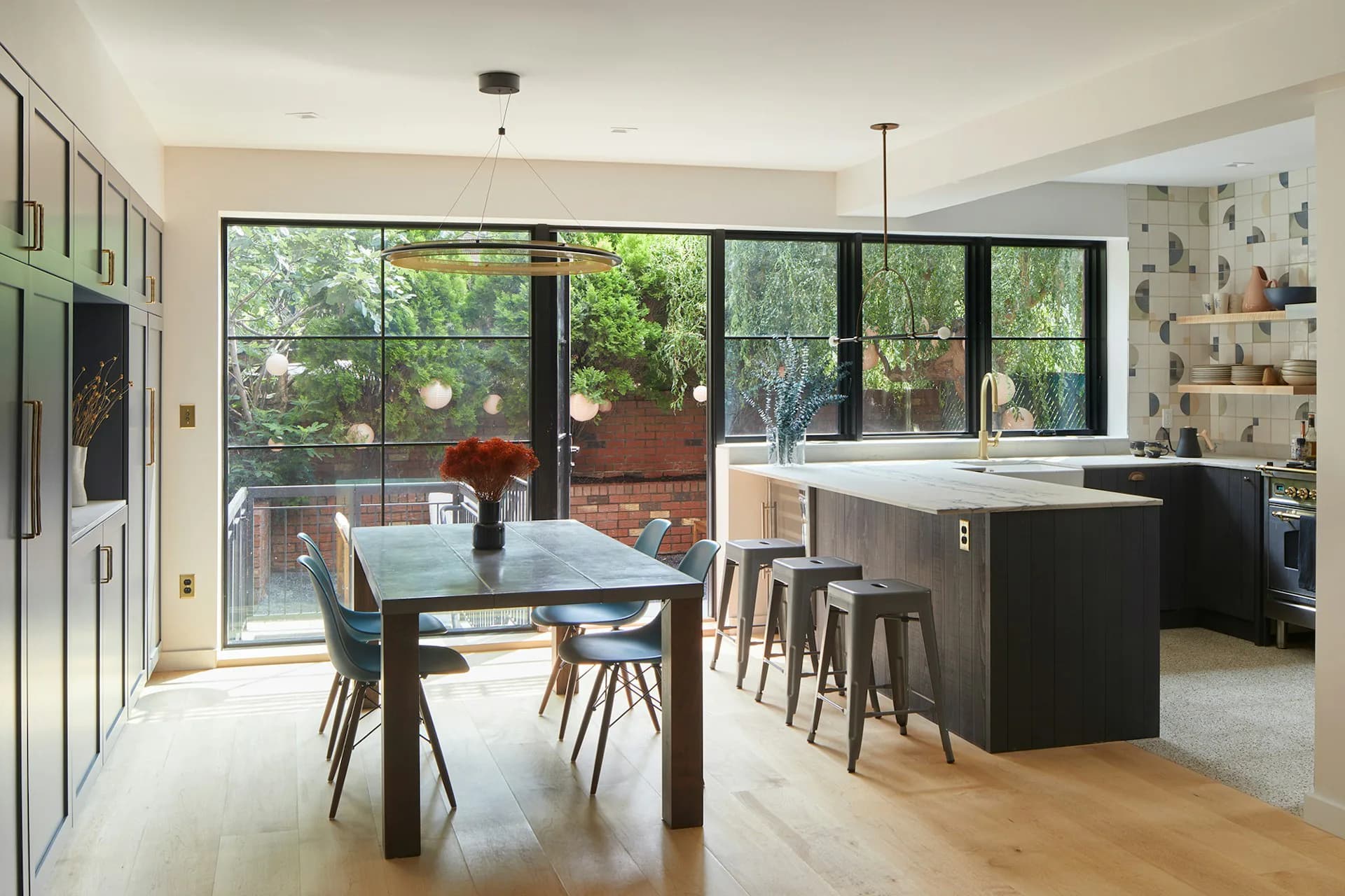 Modern open-plan kitchen and dining space with black dining table, dark cabinetry, light wood flooring, and expansive multi-panel glass doors overlooking a terrace by Krajewski Architect PLLC.