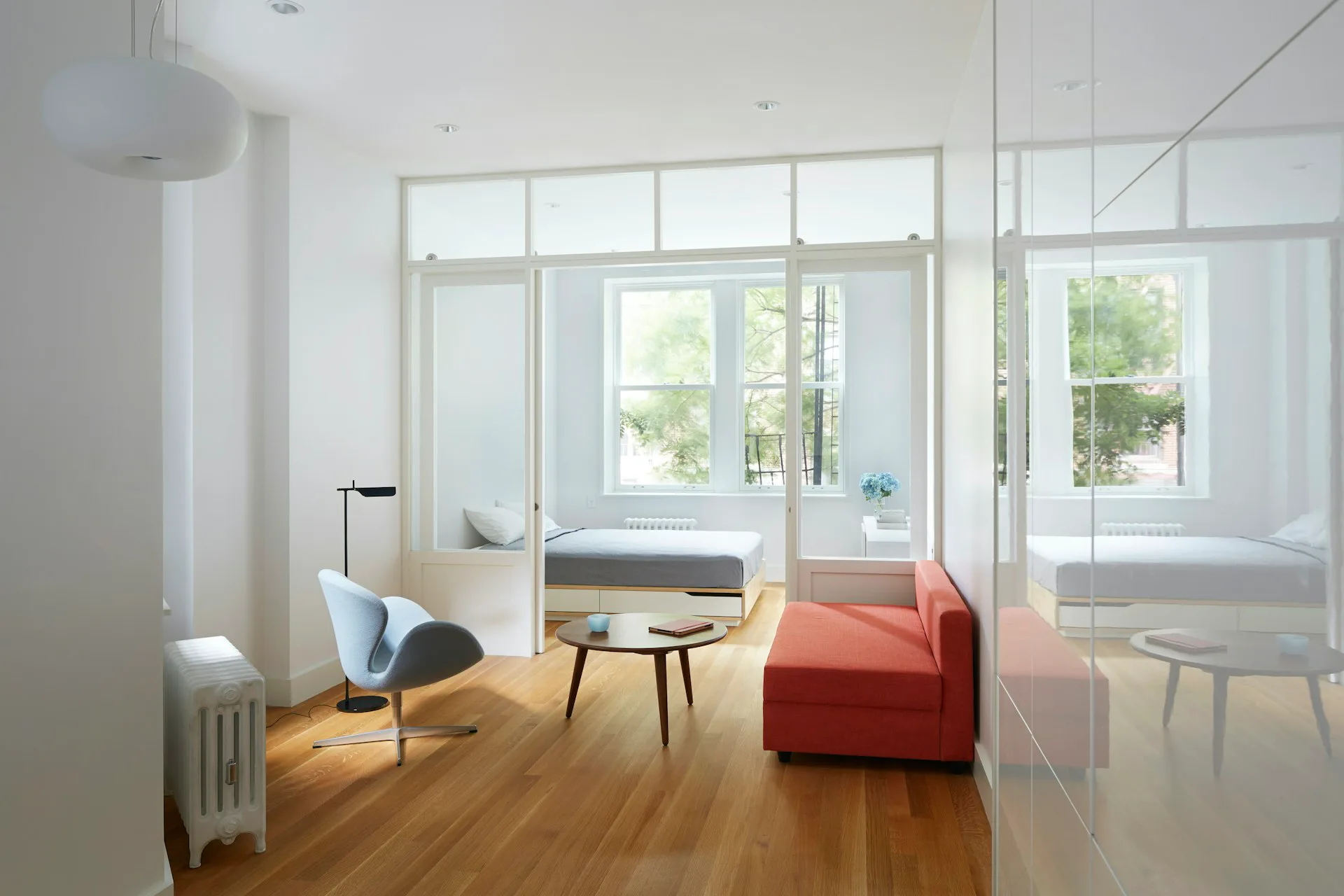Modern residential interior with glass partitions, wooden flooring, and minimalist furnishings featuring an orange sofa and light blue chair by Krajewski Architect PLLC.