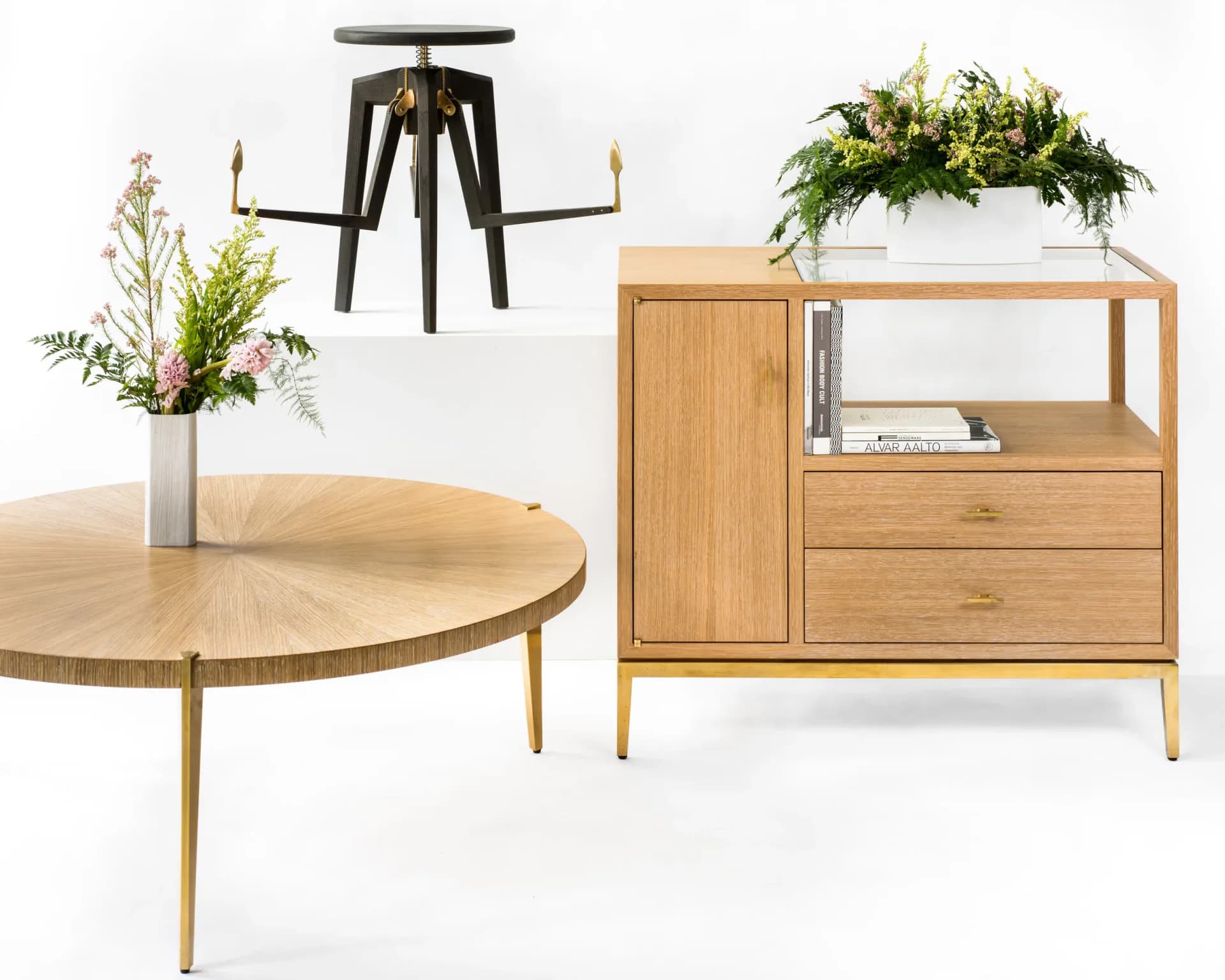 Mid-century modern furniture collection featuring a round wooden table, black sculptural stool, and oak storage cabinet with potted plants, rendered with clean lighting and neutral backdrop by KWH Furniture.