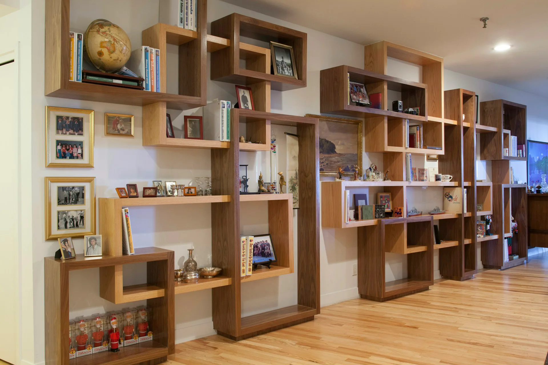 Custom wooden shelving units with varied compartments display books, decorative objects, and personal items in a bright interior with warm wood tones and white walls by +LAB Architect PLLC.