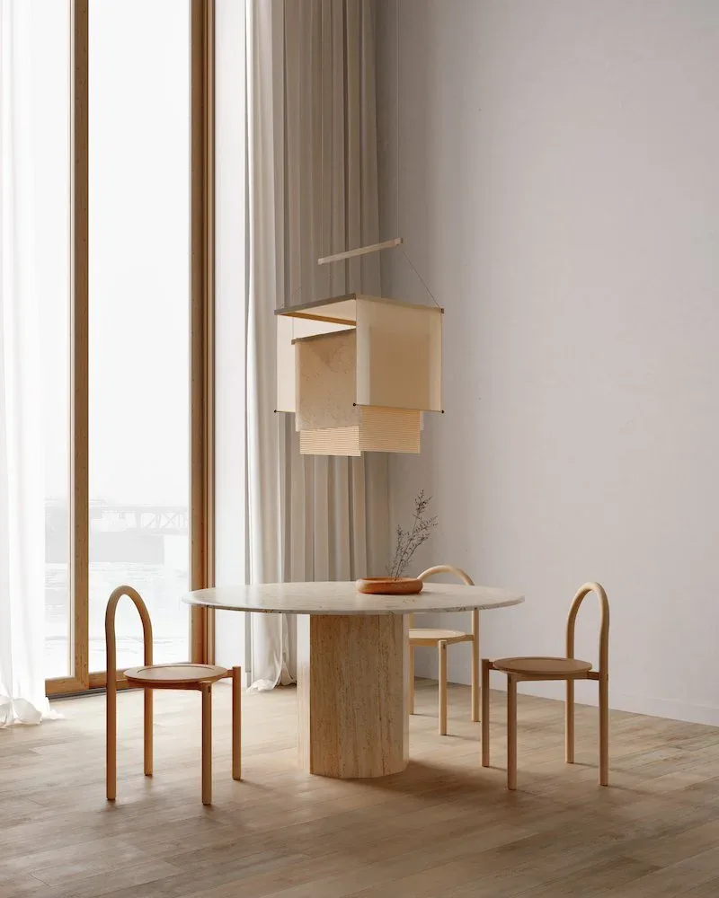 Minimalist dining space with wooden pedestal table, curved bentwood chairs, and suspended cardboard sculptural elements against floor-to-ceiling windows by Ladies & Gentlemen Studio.