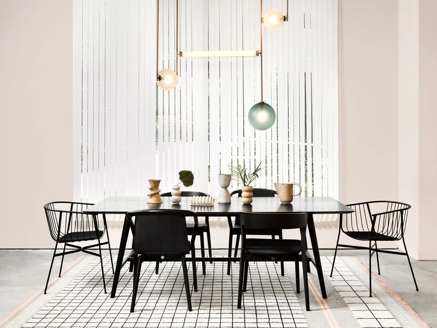 Modern dining space with black table and wire chairs, white vertical slat wall backdrop, brass pendant lights, and geometric floor pattern by Ladies & Gentlemen Studio.