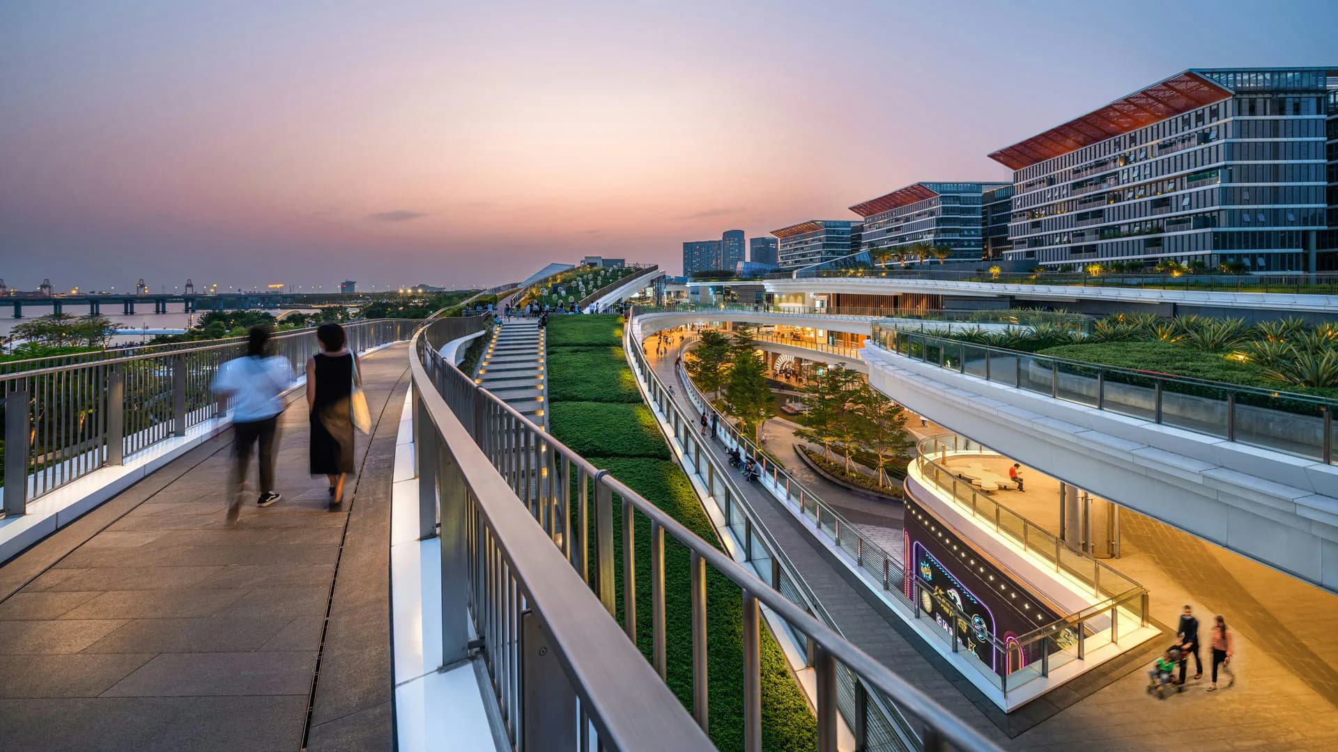 Twilight view of a modern elevated pedestrian bridge with green plantings and commercial buildings, designed by LAGUARDA.LOW ARCHITECTS.