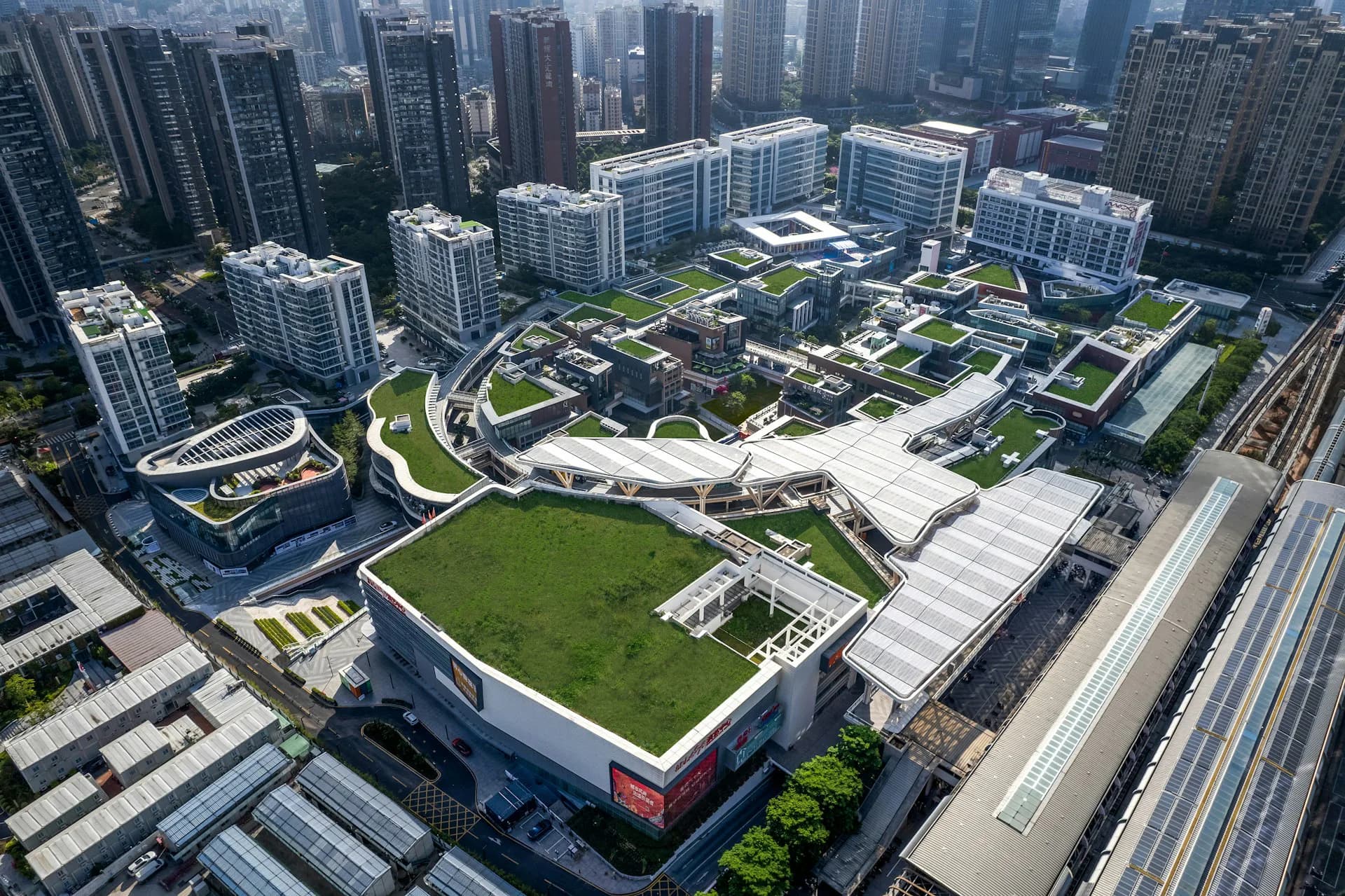 Aerial view of a modern urban plaza with green rooftop spaces, curved walkways, and integrated landscaping surrounded by high-rise buildings by LAGUARDA.LOW ARCHITECTS.