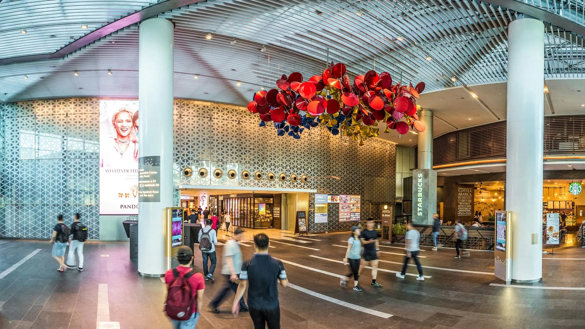 Modern airport terminal lobby with soaring white columns, geometric tile wall treatment, and dramatic suspended red floral installation by LAGUARDA.LOW ARCHITECTS.