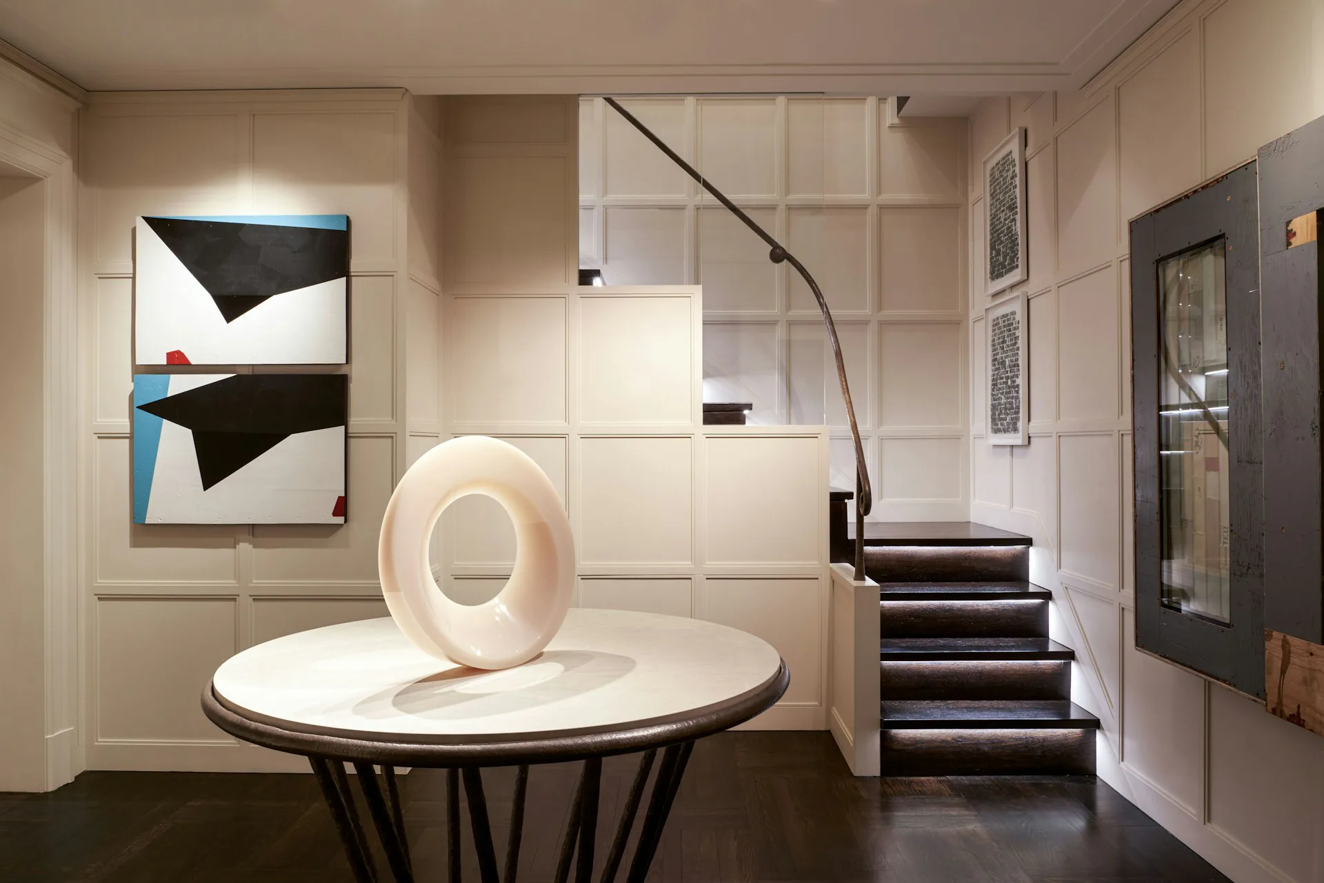 Modern entryway with cream and dark tones featuring a sculptural white circular element on a round table, geometric wall art, floating staircase, and minimalist design by Larson Architecture Works pllc.