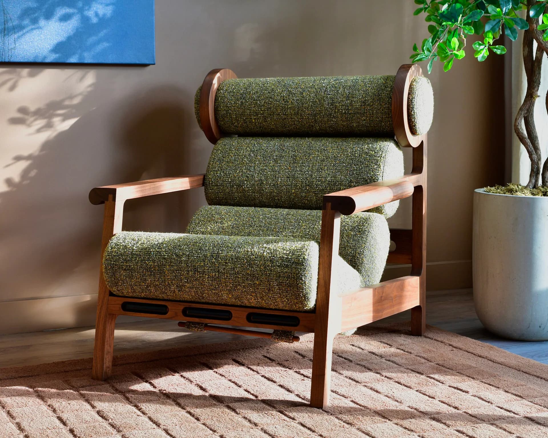 Mid-century modern lounge chair with green upholstered cushions and warm wood frame, positioned in a sunlit interior space with neutral walls and potted plants by Last Ditch Design.