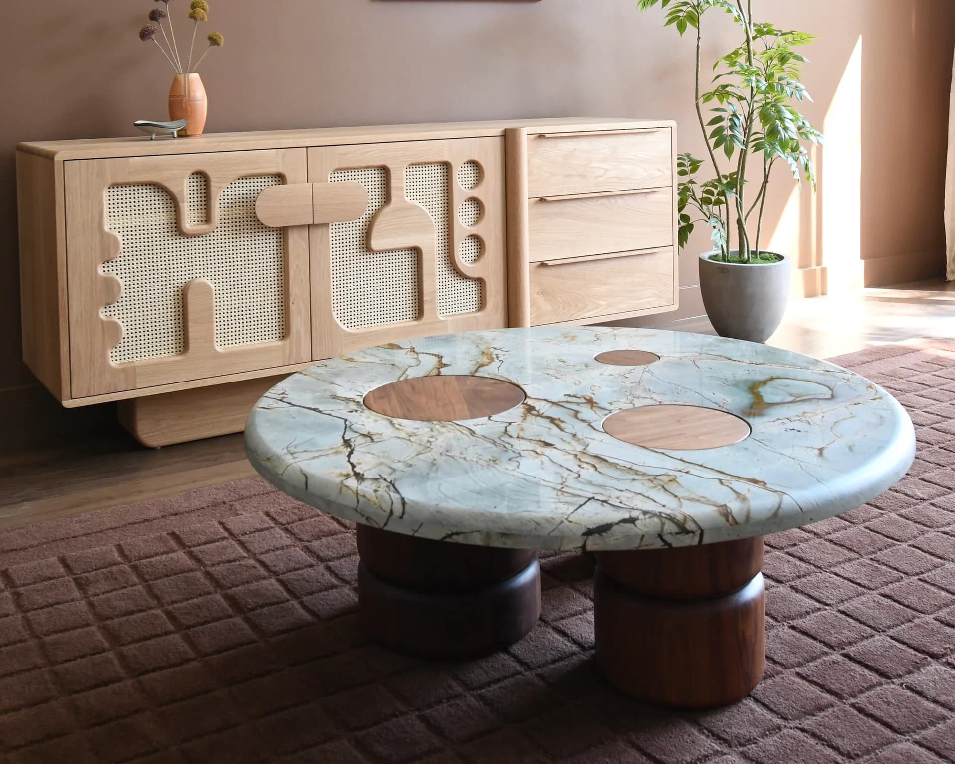 Light-filled showroom featuring a sculptural marble-top table with organic cutouts and wooden base, paired with a natural wood credenza with geometric relief detailing by Last Ditch Design.